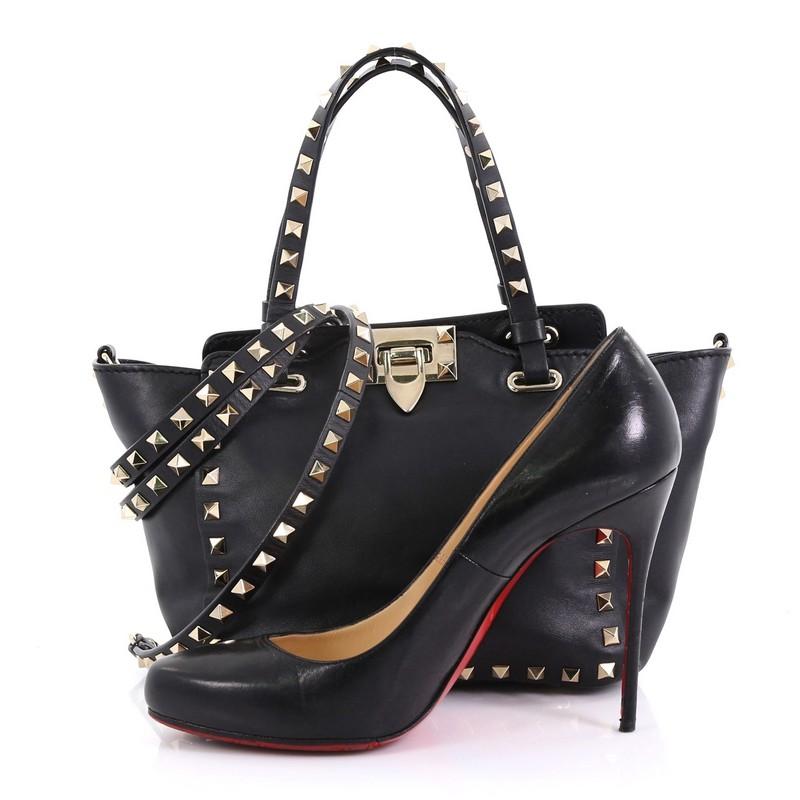 This Valentino Rockstud Tote Soft Leather Micro, crafted from black soft leather, features dual tall flat handles, pyramid stud trim details, and gold-tone hardware. Its clasp lock closure opens to a black fabric interior with side zip pocket.
