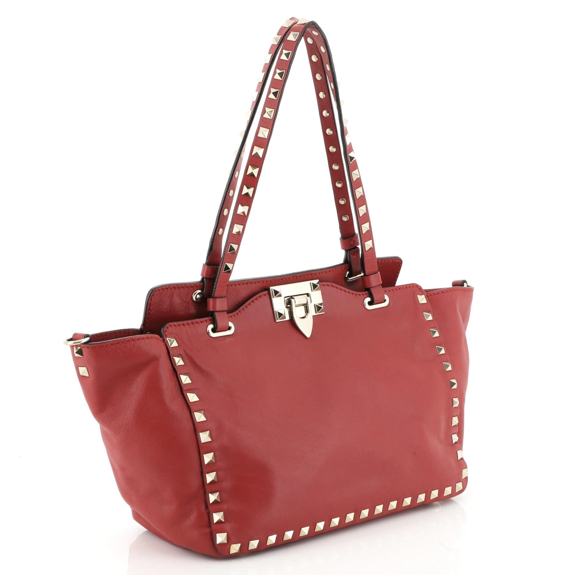 This Valentino Rockstud Tote Soft Leather Small, crafted from red leather, features dual tall flat handles, pyramid stud trim details, and gold-tone hardware. Its clasp lock closure opens to a neutral fabric interior with side zip pocket.