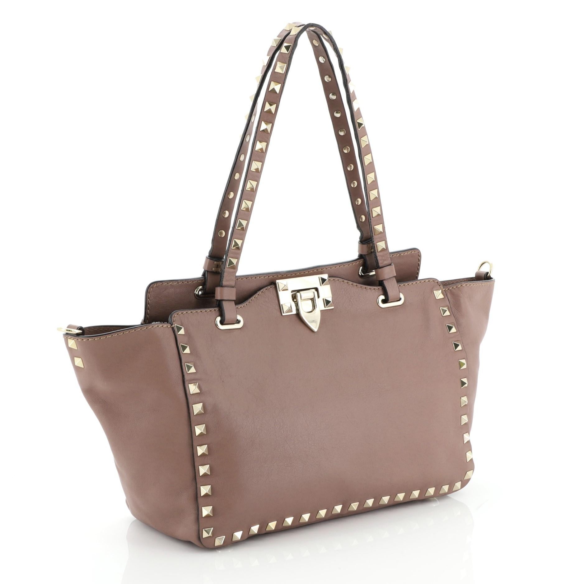 This Valentino Rockstud Tote Soft Leather Small, crafted from purple soft leather, features dual tall flat handles, pyramid stud trim details, and aged silver-tone hardware. Its clasp lock closure opens to a brown fabric interior with side zip