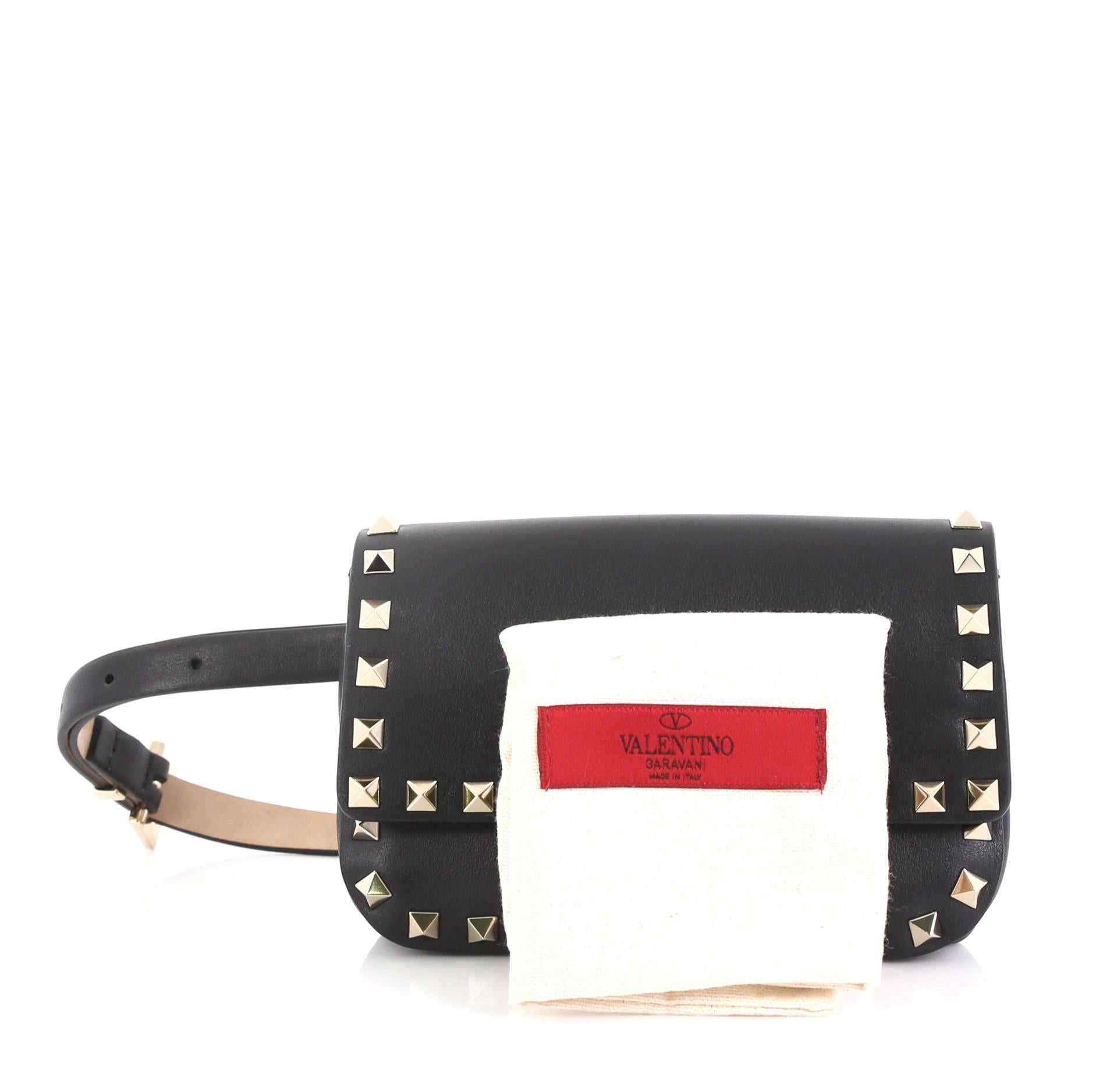 This Valentino Rockstud Waist Bag Leather, crafted from black leather, features pyramid stud embellishments, adjustable leather belt strap, and gold-tone hardware. Its magnetic snap closure opens to a black fabric interior. 

Estimated Retail Price: