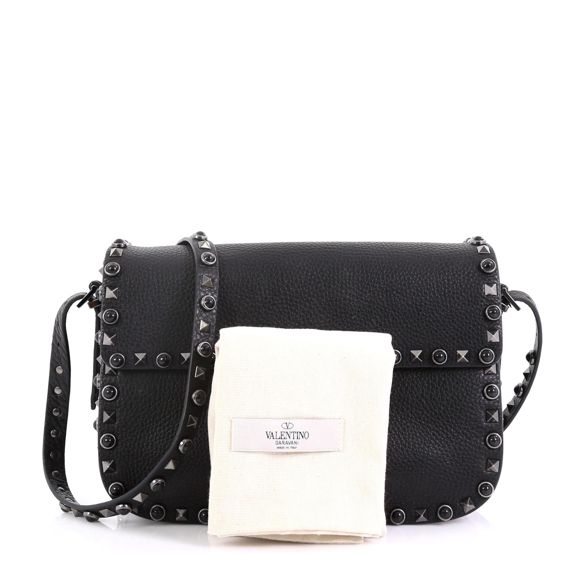This Valentino Rolling Rockstud Crossbody Bag Leather with Cabochons Medium, crafted from black leather, features a leather crossbody strap, rockstud and cabochon trim, and gunmetal-tone hardware. Its flip-lock closure opens to a black suede
