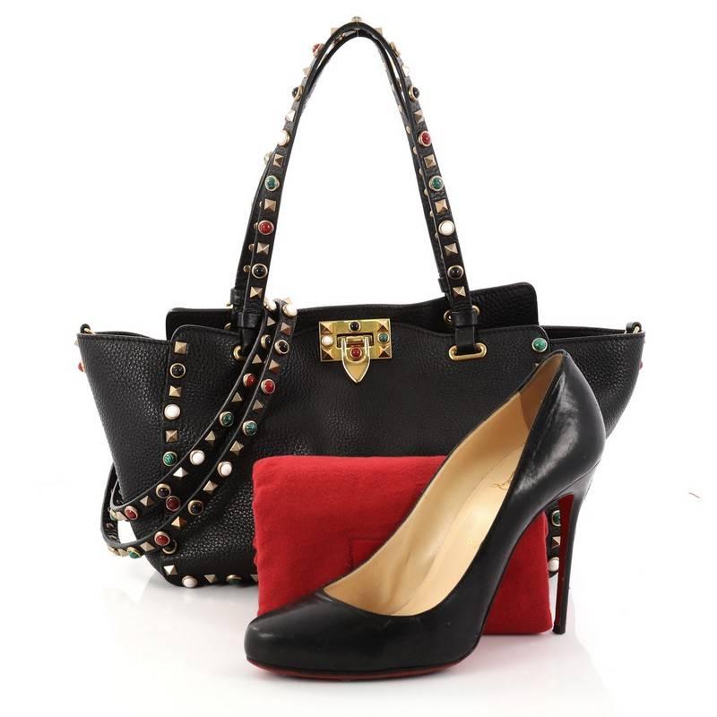 This authentic Valentino Rolling Rockstud Tote Leather with Cabochons Small mixes chic styling with luxurious flair. Crafted from black leather, this stand-out bag features studded dual-flat leather handles, signature bronze rockstud and multicolor