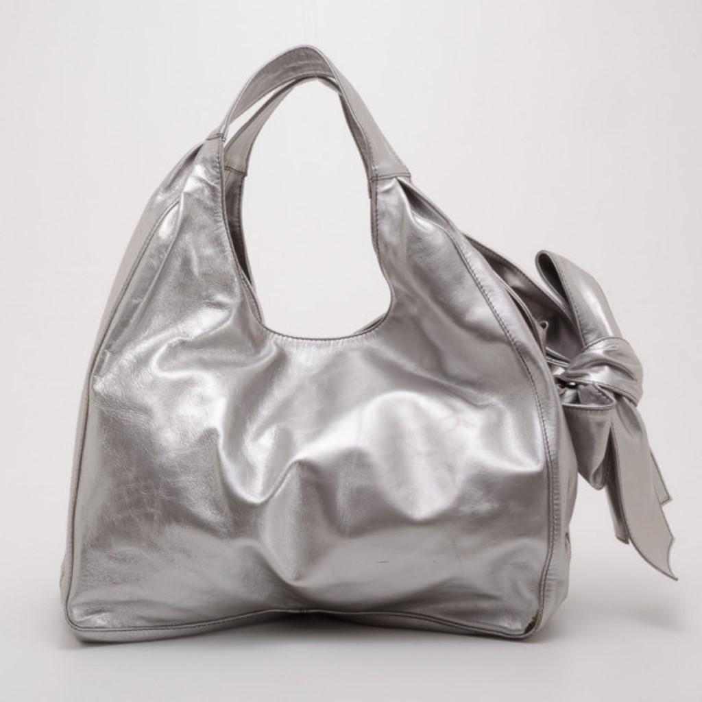 Look fabulous while carrying this feminine yet modern silver Nuage by Valentino. The hobo style bag is crafted from metallic silver nappa leather that is accented with an over-sized bow and comfortable shoulder straps. Its spacious interior is lined