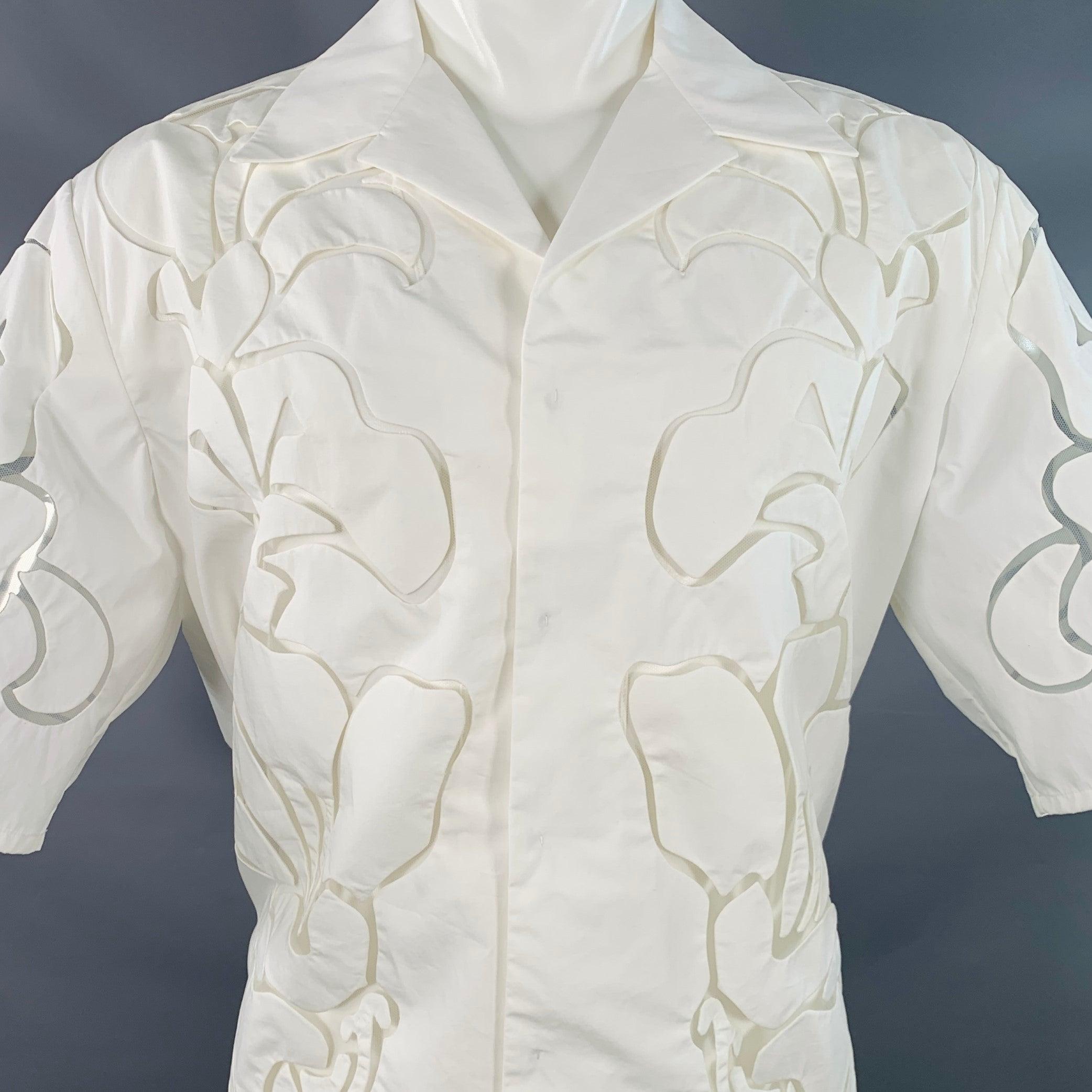 Chemise à manches courtes VALENTINO 2021 en coton blanc mélangé à de la soie, avec un subtil motif de dentelle florale, un col ouvert et une fermeture à bouton caché. Fabriqué en Italie. Très bon état. Signes mineurs d'usure. 

Marqué :   46