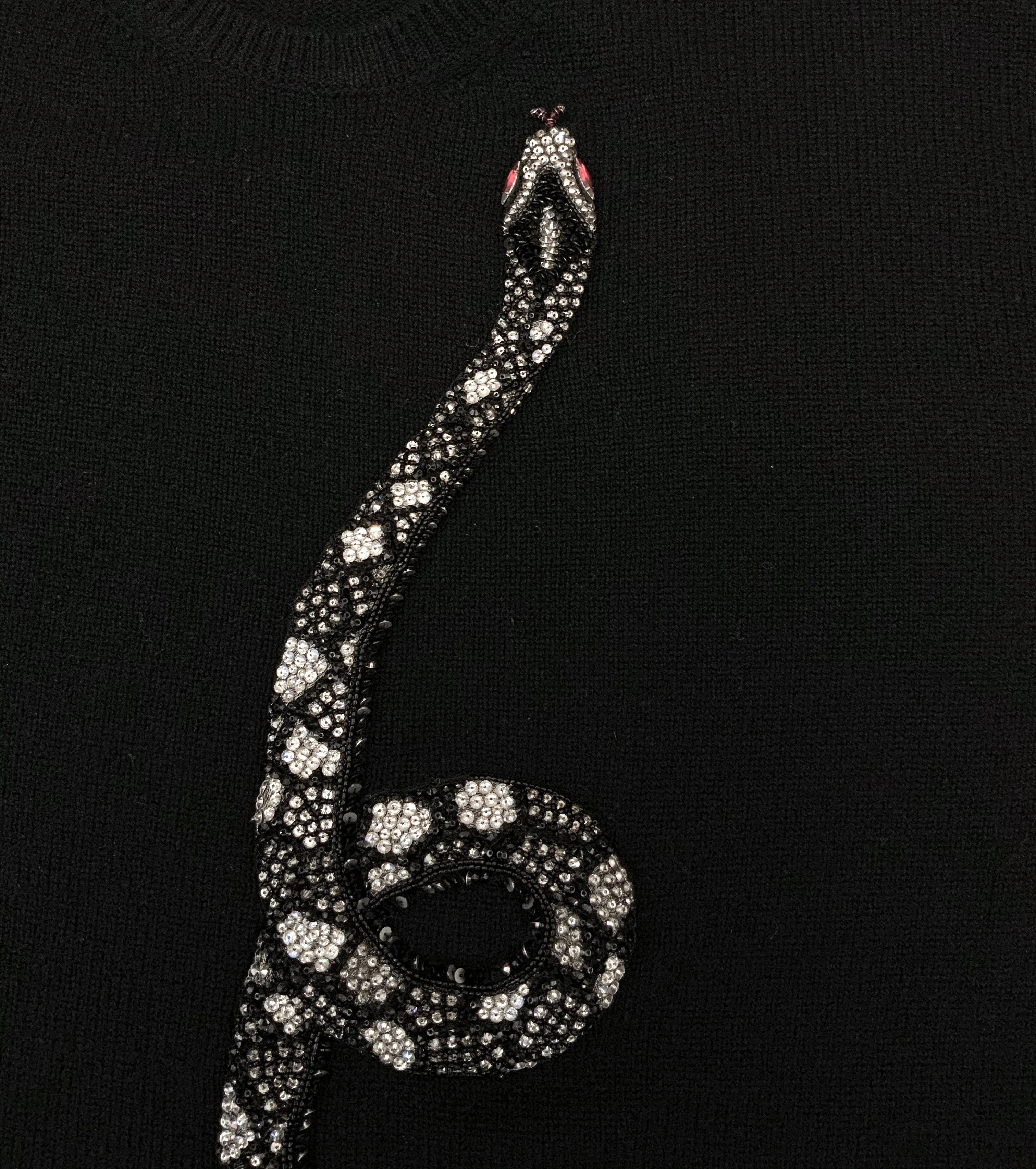 This Limited Edition back cashmere sweater from the house of Valentino shows an embroidered snake design. 
This snake detail is a re-edition of an archival embroidered motif from the Haute Couture FW 1971-72 collection 

Collection: Re-edition of
