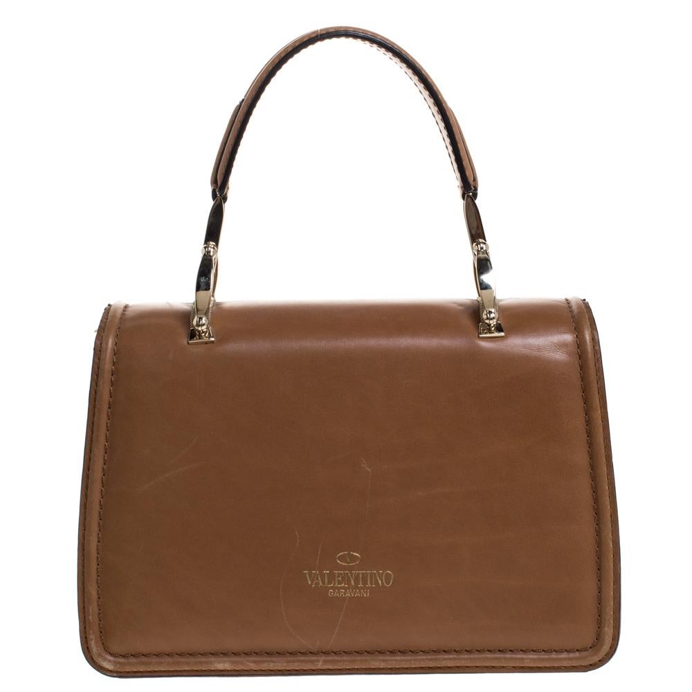 This sleek and smart bag from Valentino is a must-have. Crafted in Italy, it is made from quality leather. It comes in a versatile shade of tan. It is styled with a top handle, a detachable shoulder strap and a front flap with bow detailing. The bag