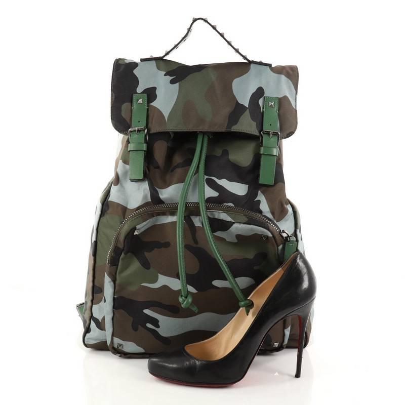 This authentic Valentino Top Flap Backpack Camo Nylon Large is a stylish backpack perfect for on-the go moments. Crafted in green camouflage nylon, this practical bag features dual leather shoulder straps with stud detailing, green leather trims,