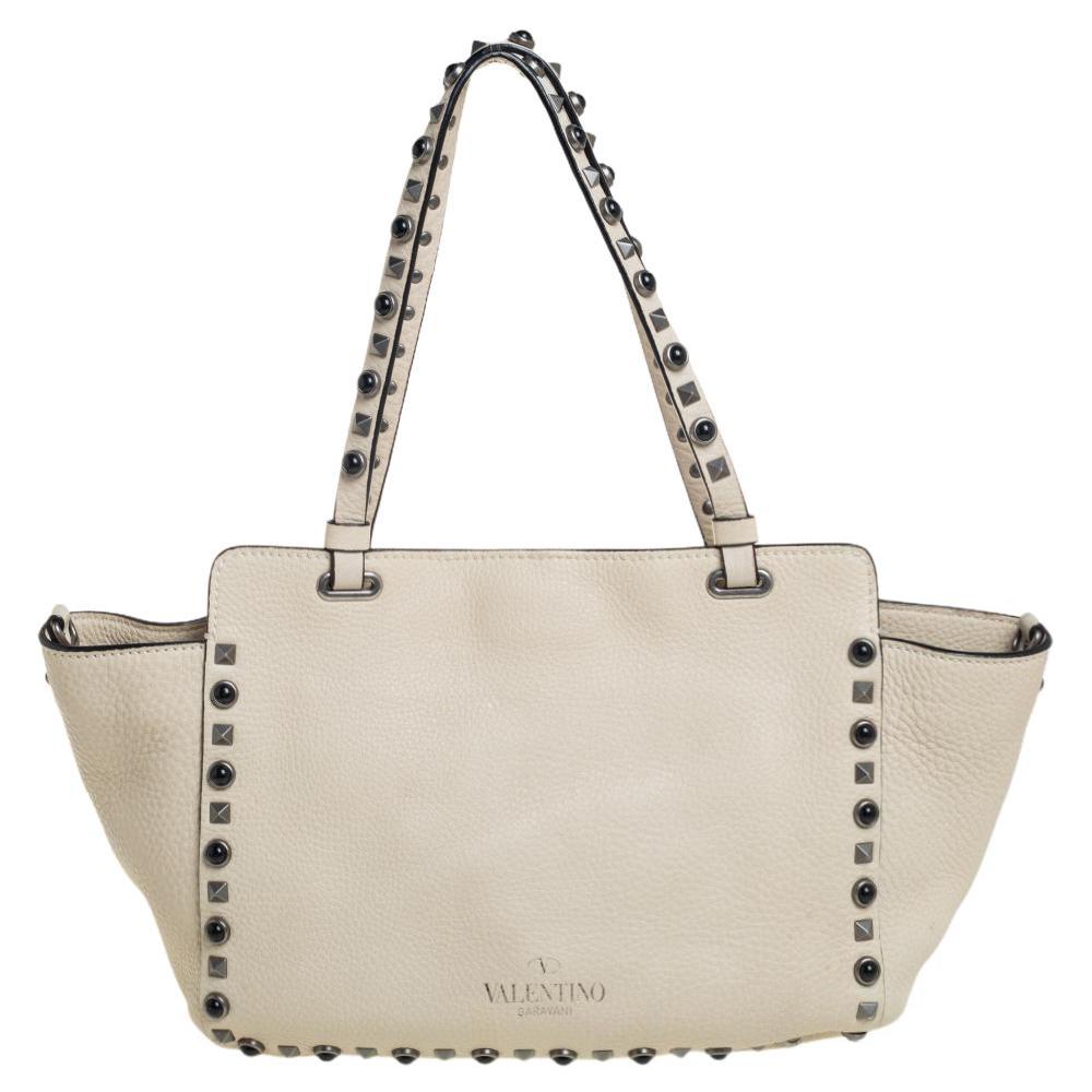 Valentino brings you this super-stylish tote that carries a design that will surely grab the attention of your onlookers. It has a vanilla leather exterior decorated with the signature pyramid Rockstuds. The tote is complete with a spacious suede