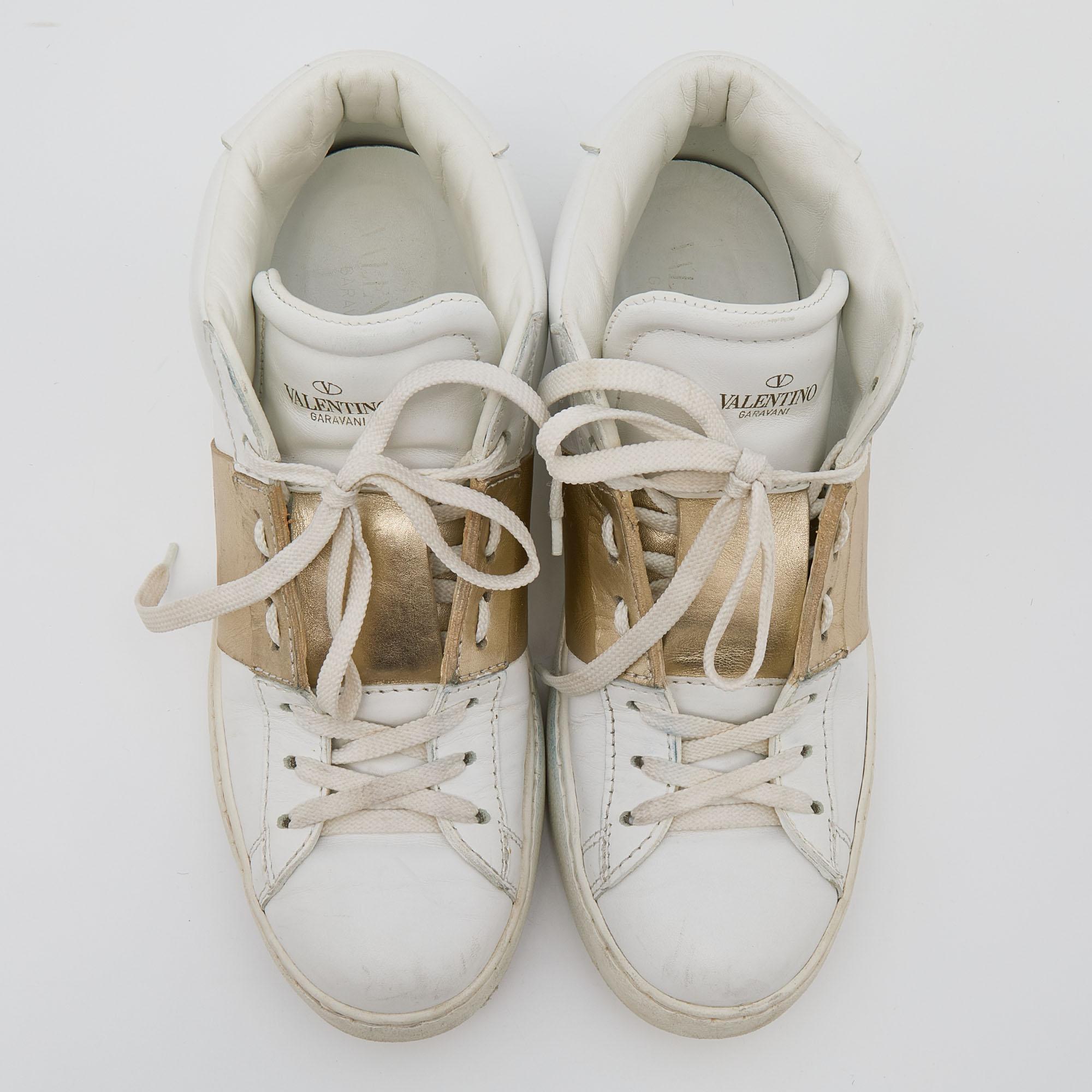 These white Valentino leather sneakers are trendy and casual with a gold strap detailing on the quarter panel. Signature Rockstuds are present on the rear midsoles. The high-top silhouette, rubber soles, and soft insoles make them a favorite for the