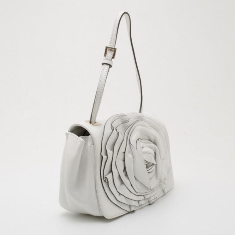 Decorated with a prominent white leather rosette on its big flap, this Valentino Shoulder Bag is sure to grab lots of compliments. This spacious bag holds an open patch pocket and an extra bold monogrammed pocket. It's fastened to an adjustable