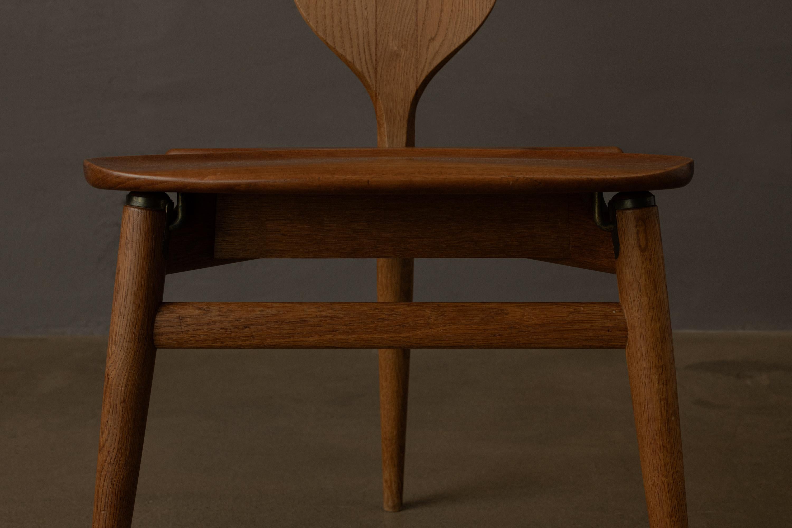 Designed by Hans J. Wegner, crafted in Denmark, it features a contoured back shaped like a coat hanger, a gently curved teak seat with integrated storage, and tapered legs.