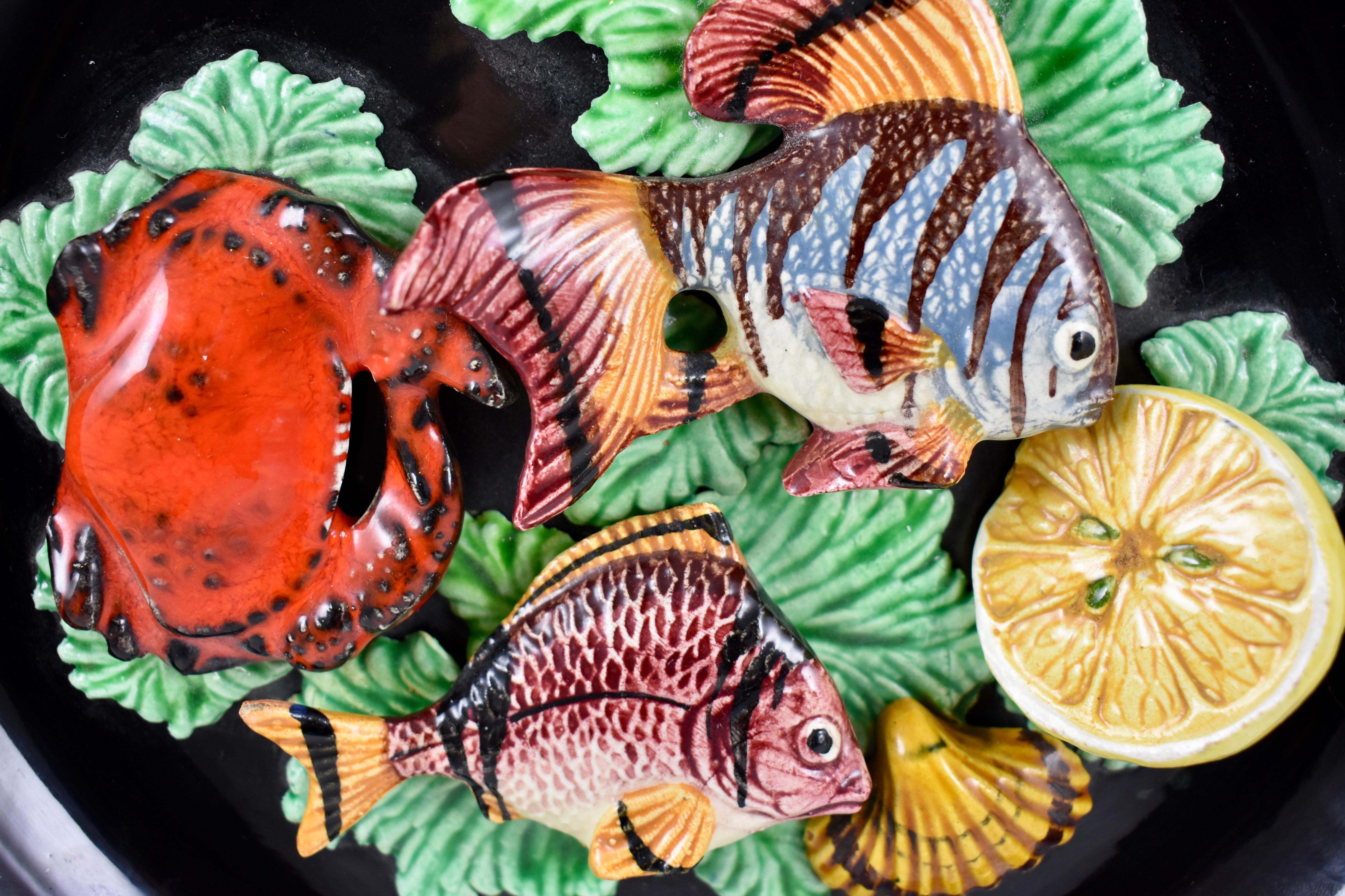 A Palissy style Provençal majolica trompe l’oeil wall plate from Vallauris, Cote d’Azur, Mid-Century Modern Era, France, circa 1950s.

A heavy piece, a matte black glazed earthenware body, showing brightly colored, dimensional seafood found in the