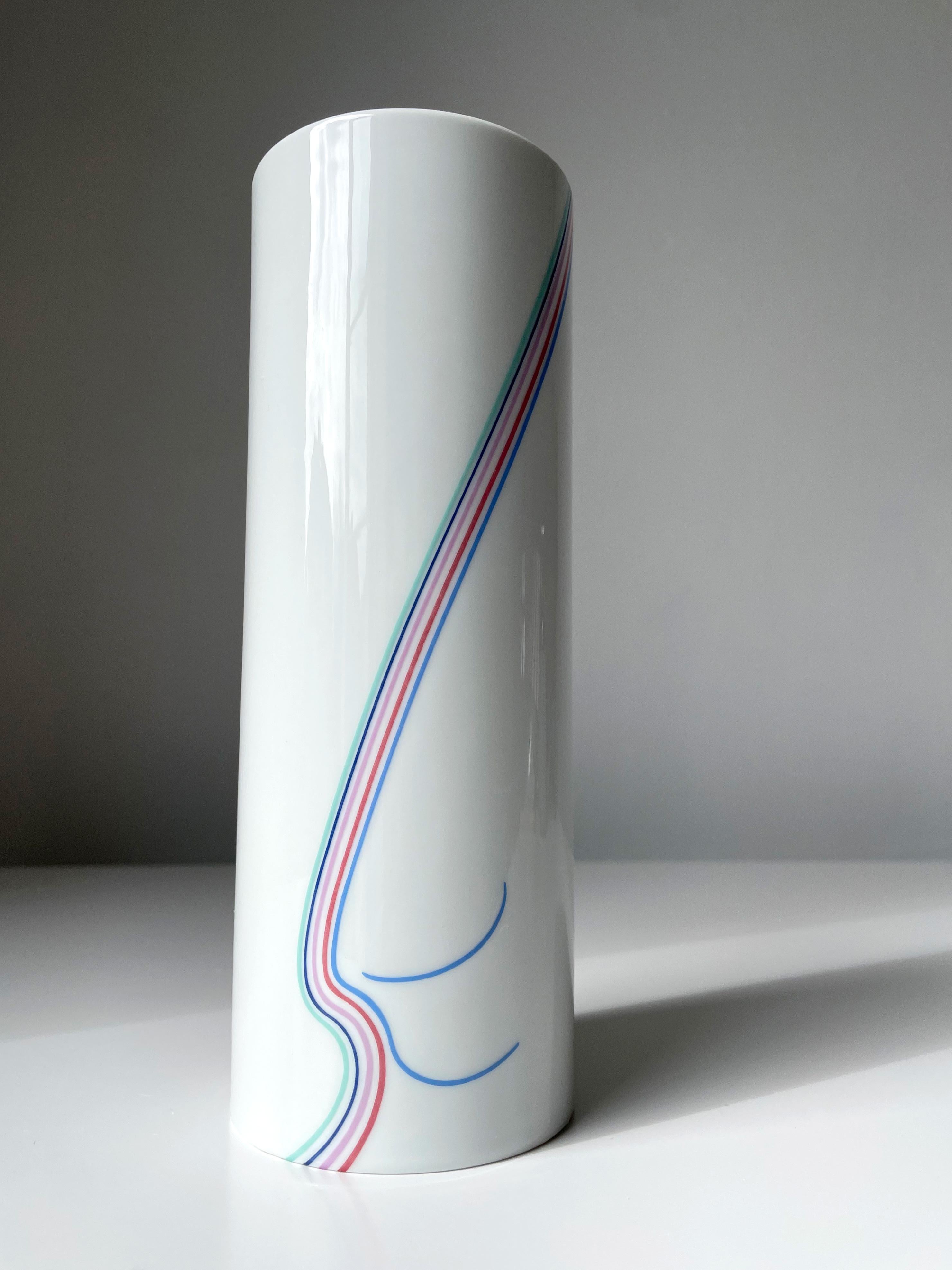 Vaso in porcellana bianca lucida a forma di cilindro della serie Rainbow disegnata da Bertil Vallien per Rörstrand negli anni Ottanta. Linee pastello vorticose su due lati nei colori menta, rosa, rosso, blu chiaro e scuro. Completamente vetrato.