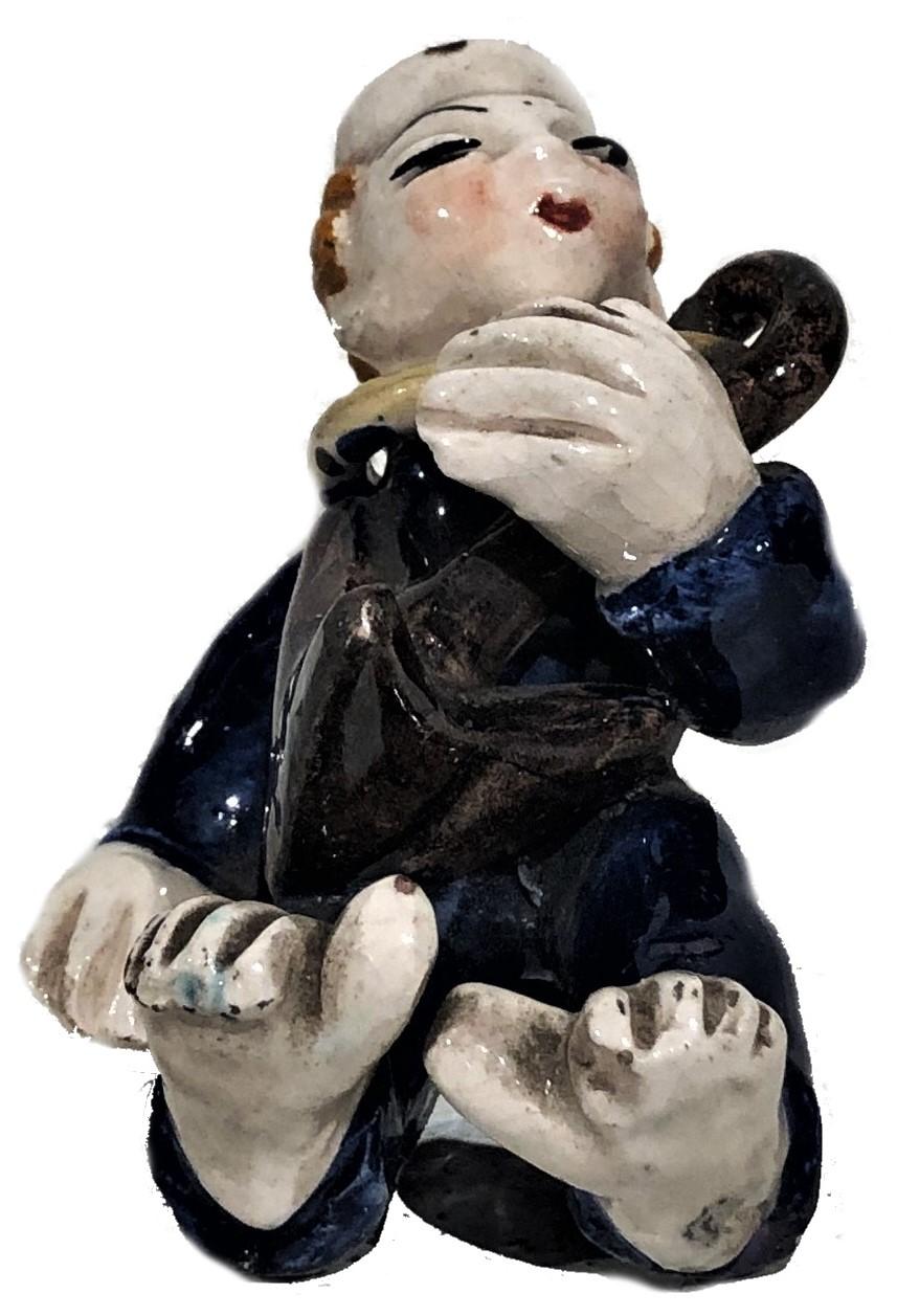 À PROPOS DE
Cette figurine de table humoristique en céramique représente un marin ivre allongé sur le dos. Autour de son cou, il porte un anneau de métal avec une ancre. 

MARQUES
Signé sur la fesse gauche : 