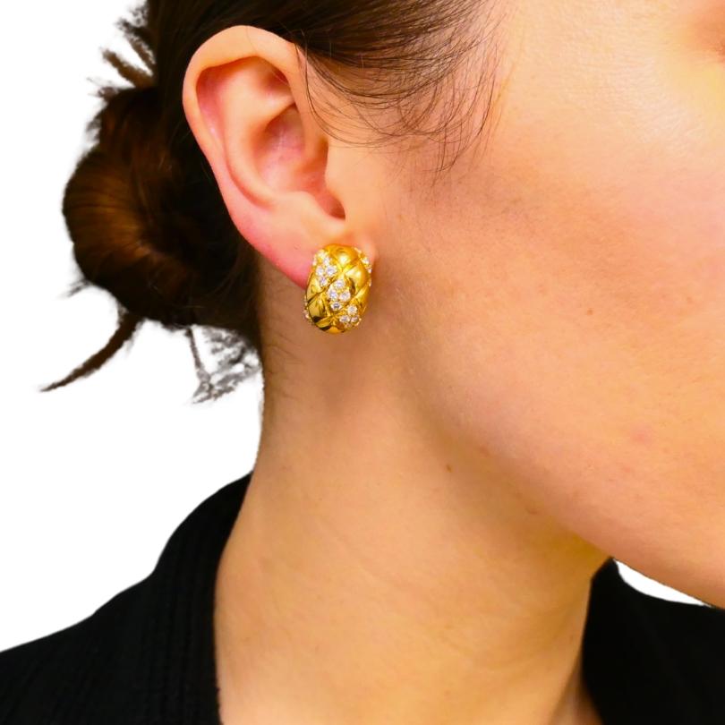 Un paio di orecchini huggie in oro 18k e diamanti di Van Cleef & Arpels.
Gli orecchini hanno un design trapuntato che aggiunge una texture e una profondità interessanti. All'interno del modello arrotondato sono incastonati gruppi di diamanti che