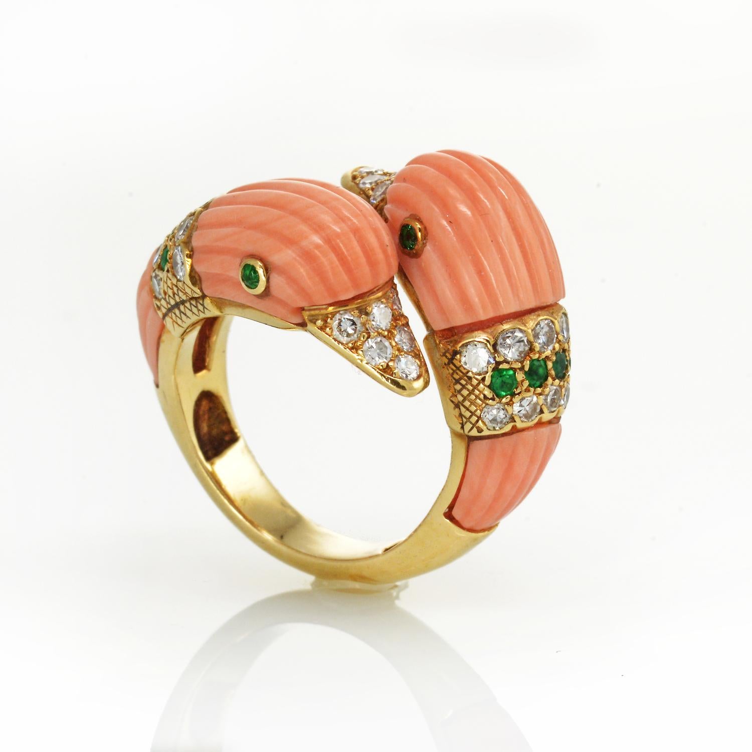 A CORAL, DIAMOND AND EMERALD RING, BY VAN CLEEF & ARPELS, CIRCA 1965.

 Designed as two opposing carved corallium rubrum duck heads, each with a diamond-set beak, circular-cut emerald eyes and circular and single-cut diamond collars, signed VCA,