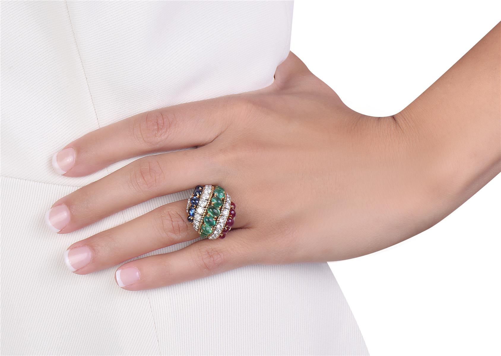 This 1960 circa Van Cleef & Arpels cocktail ring features 36 round brilliant cut diamonds weighing approximately 3.15 carats total, five oval cabochon rubies, six oval cabochon sapphires, and nine oval cabochon green emeralds set in 18K yellow gold