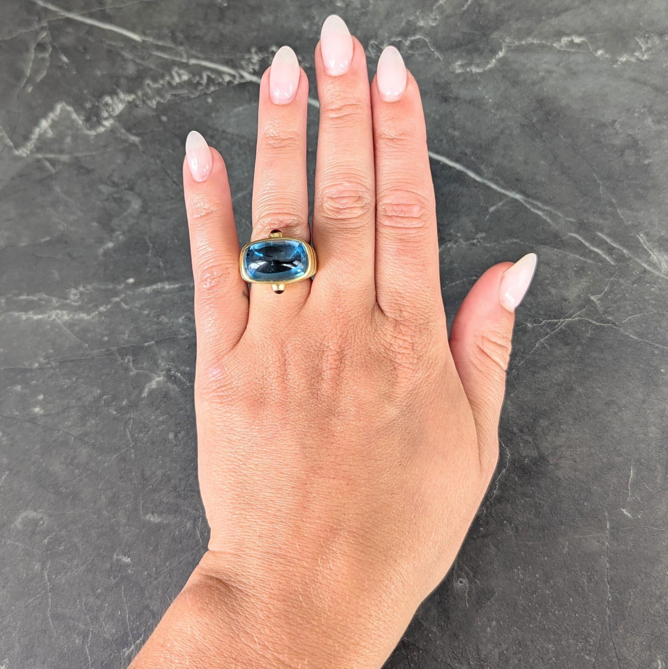 Designed as a dome shaped form centering a cushion shaped topaz cabochon
Measuring 17.0 x 11.0 mm - transparent medium vibrant blue in color
Bezel set east to west with a grooved fanning gold surround
Accented by oval shaped citrine cabochons bezel