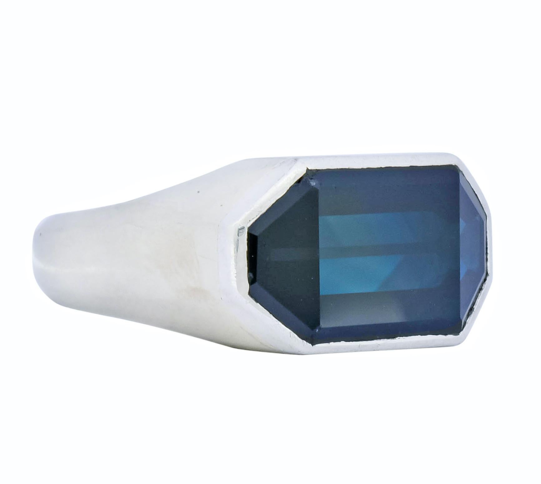 Centering a fancy cut elongated octagonal sapphire weighing approximately 9.00 carats, transparent and a dark inky blue with no indications of heat

Bezel set in platinum within a white gold mounting wherein shoulders and stone taper at a sharp,