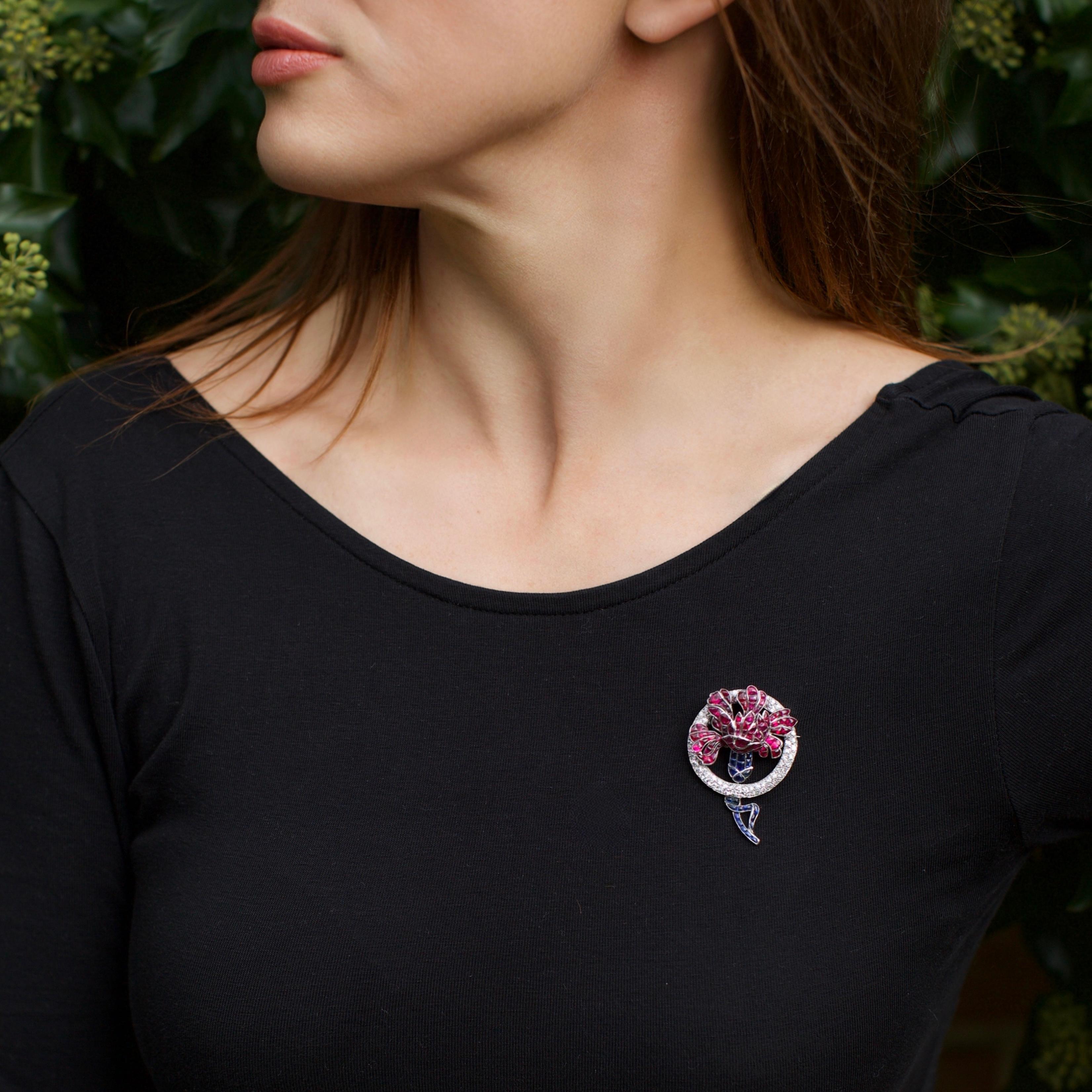 Spilla Van Cleef & Arpels Art Deco disegnata come una testa di fiore stilizzata, con incastonati rubini a forma di petali e zaffiri a forma di gambo e nastro. Il motivo floreale centrale è incorniciato da un cerchio circolare di diamanti