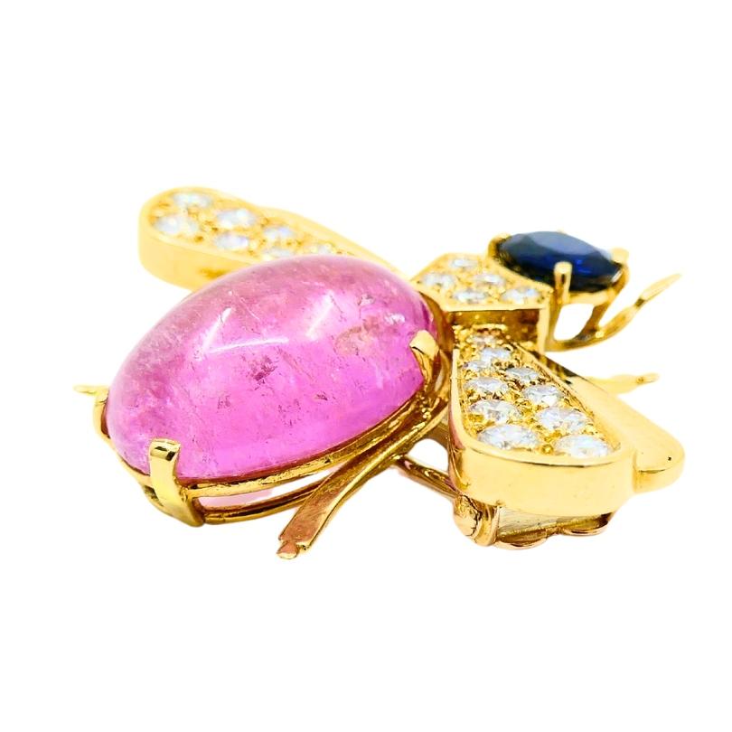 A charming Van Cleef & Arpels bee brooch, crafted in 18k gold, features pink tourmaline,
diamonds, and sapphire.
The bee’s body has a striking pink tourmaline cabochon as its central gemstone. The tourmaline
giving it a soft glow, while shimmering