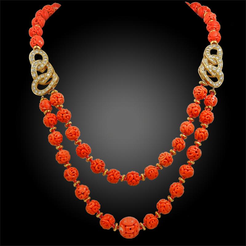 A stunning suite by Van Cleef & Arpels comprising a necklace and earrings. The necklace is exceptionally made with a double row of vibrant carved coral beads and 18k gold interlocking rings embellished with brilliant diamonds. The earrings are of