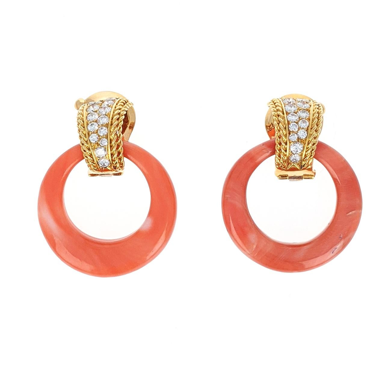 This lovely pair of ear clip earrings by Van Cleef and Arpels features two pieces of orangy-pink carved coral hoops suspended from 18 karat yellow gold clips. The clips are set with 26 round brilliant-cut diamonds with a total diamond weight of
