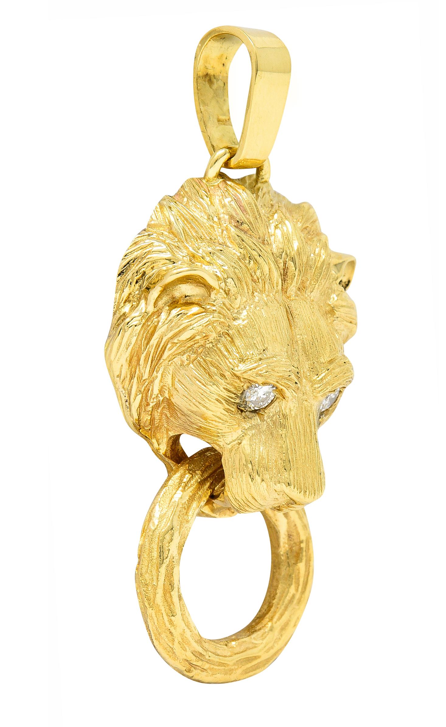 Designed as a highly rendered lion head with a deeply grooved fur texture throughout. Holding an articulating ring between its teeth - with grooved texture. Featuring round brilliant cut diamond eyes - flush set. Weighing approximately 0.20 carat