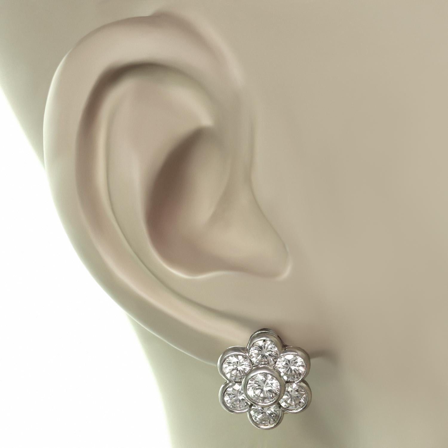 These beautiful Van Cleef & Arpels earrings feature a six petal design crafted in platinum and bezel-set with brilliant-cut round E-F-G VVS1-VVS2 diamonds - the two center diamonds weigh an estimated 0.50 carats and the 12 surrounding diamonds weigh