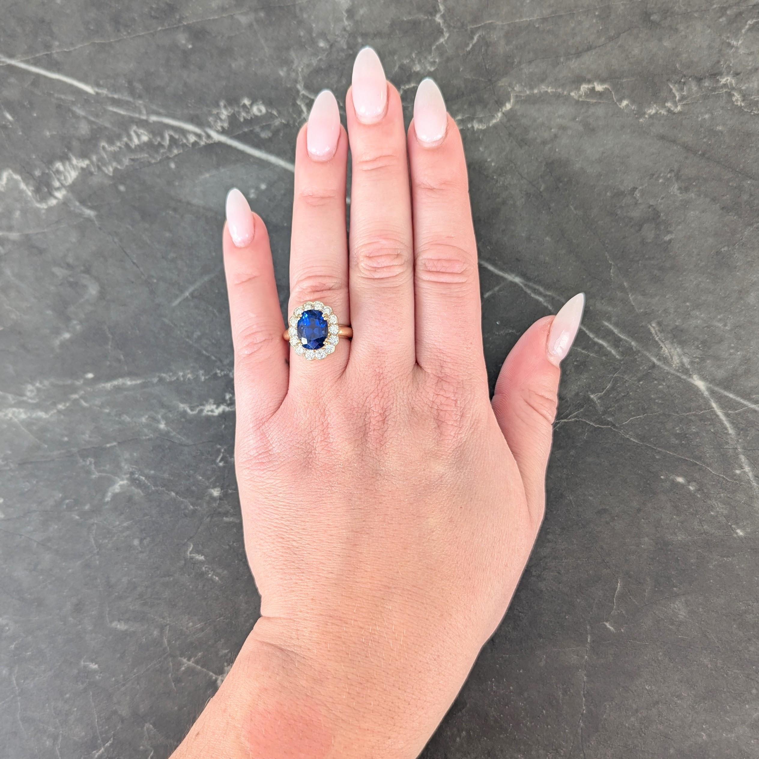 Centering a cushion cut sapphire weighing 5.65 carats - transparent vivid royal blue in color
Burmese in origin with no indication of heat treatment 
Set by split prongs with a scalloped halo surround of round brilliant cut diamonds
Weighing