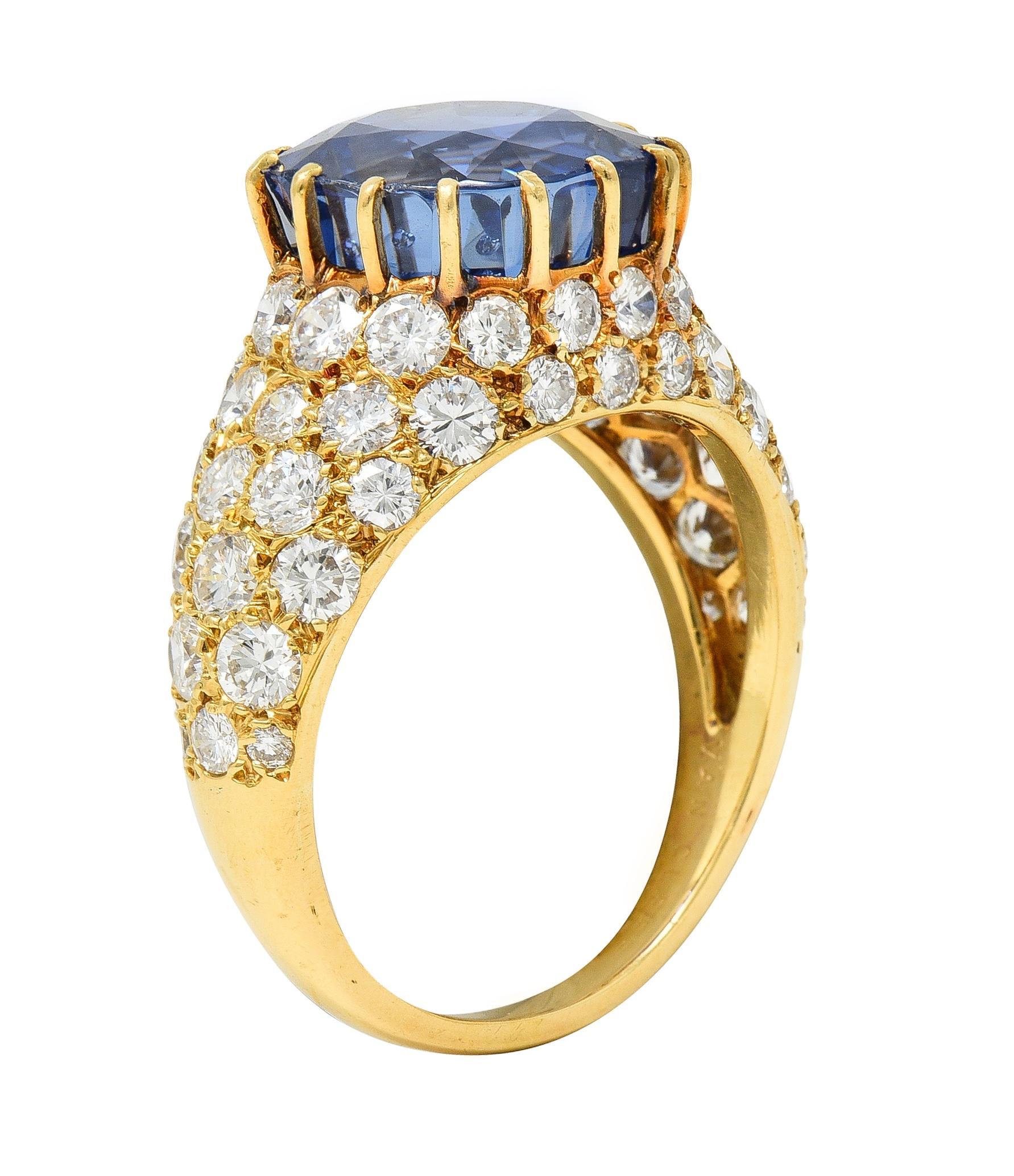 Centering a cushion cut sapphire weighing 9.43 carats total - transparent medium blue 
Natural Sri Lankan in origin with no indications of heat treatment 
Set with talon prongs with a domed gold surround
Pavé set with round brilliant cut diamonds