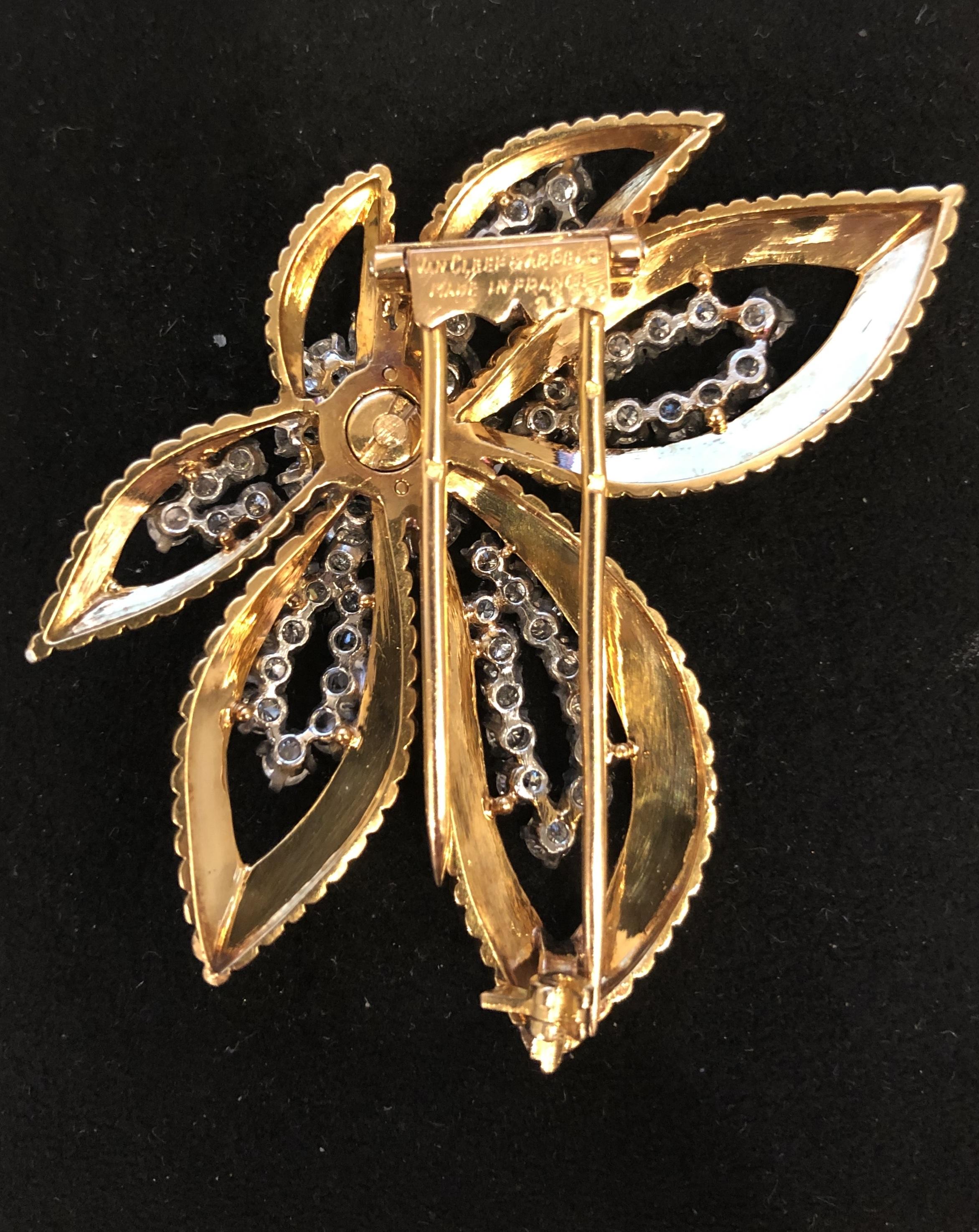A French Mid-20th Century 18 karat gold and platinum brooch with diamonds and emerald by Van Cleef & Arpels. The brooch is done in a dynamic floral motif, with textured gold petals lined with round brilliant cut diamonds and centering on a cabachon