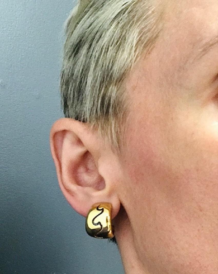 A pair of Van Cleef & Arpels huggie earrings crafted of 18k gold. 
These gold Van Cleef earrings have a slightly domed shape with the abstract, curving cutout detail. This design runs across the surface, adding a sense of movement. The cutout has an