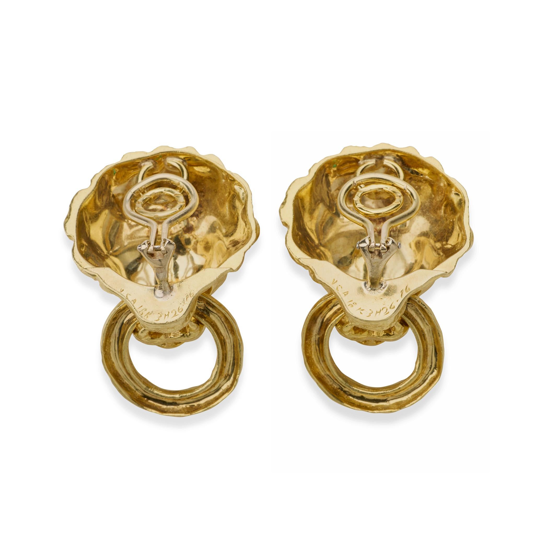 Created in the 1960s, these Van Cleef & Arpels lion clip earrings are formed of 18K gold and emeralds. Each is designed as a high-relief lion mask with emerald eyes, and suspending a freely-moving textured ring in its open mouth (earclip findings