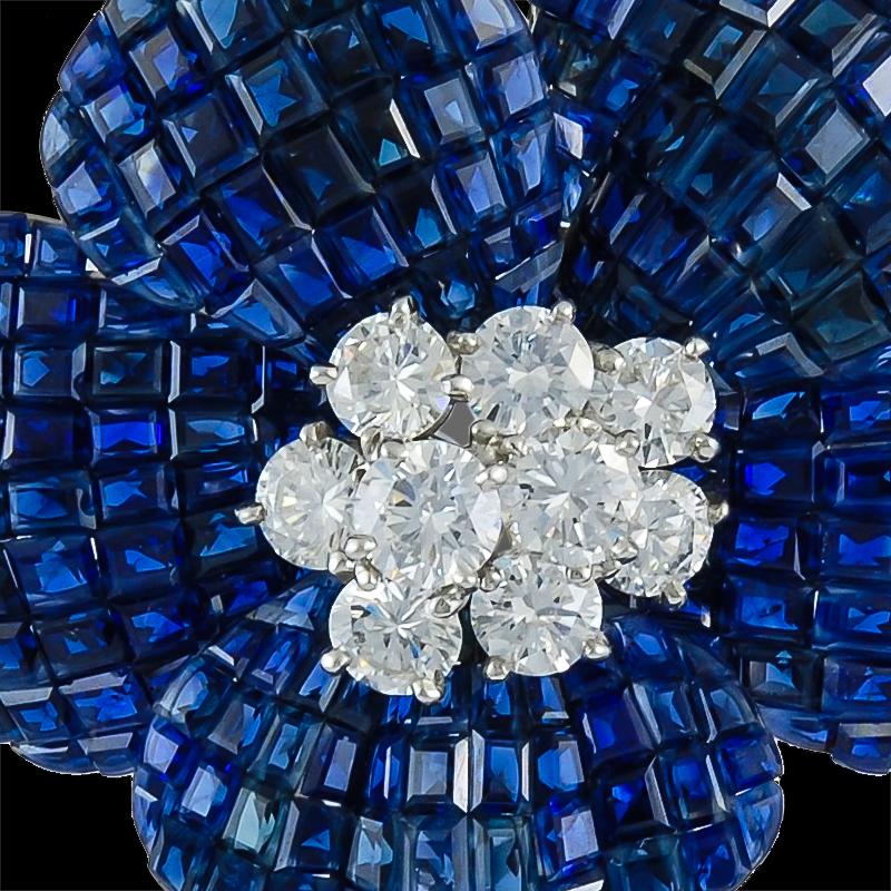 A platinum diamond and mystery-set sapphire flower pin designed as a calibre-cut sapphire flower, centering upon diamond cluster pistil, extending a baguette-cut diamond stem and marquise-cut diamond leaves, exquisitely mounted in platinum.
The