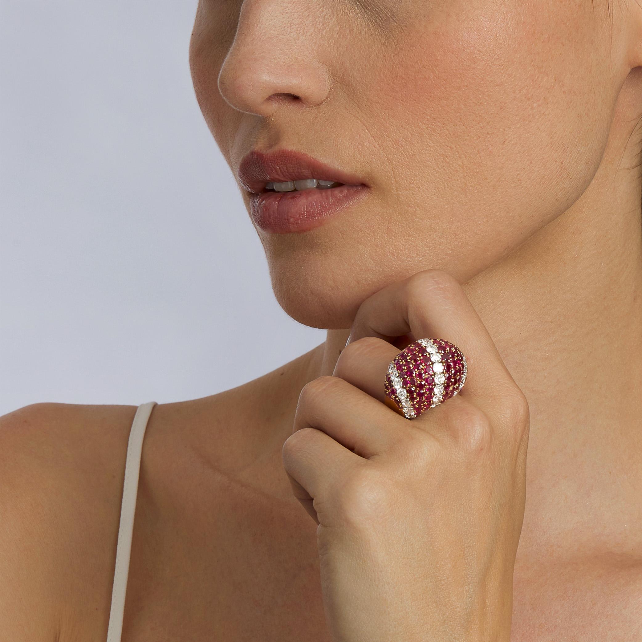 Created in the 1960s, this 18K gold and platinum bombé ring is set with rubies and diamonds. The high volume bombé form is set with fields of circular-cut rubies, interspersed with three arced lines of round brilliant-cut diamonds. This exuberant