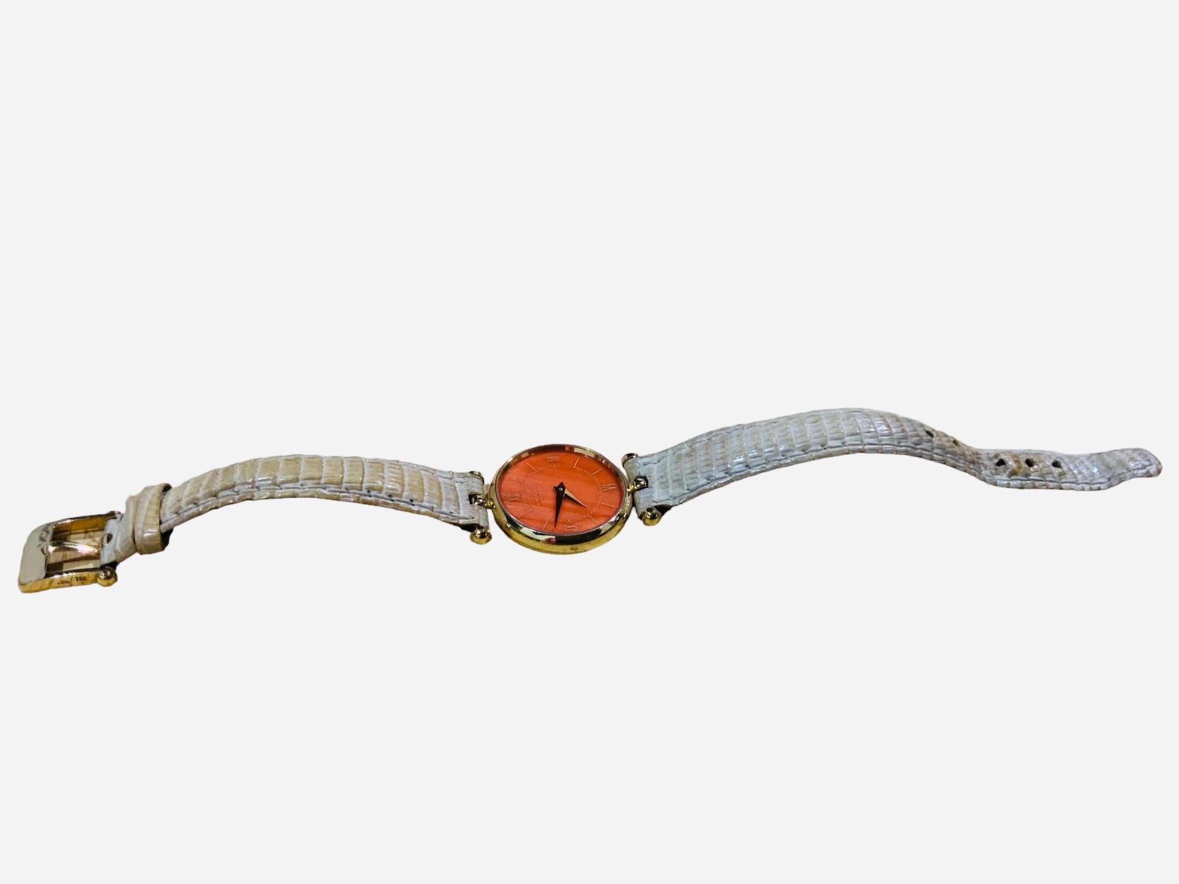 Il s'agit d'une montre-bracelet Van Cleef & Arpels Pierre Arpels pour femme. Elle présente un boîtier rond en or 18 carats/750 avec un cadran de couleur corail comportant des chiffres romains et des aiguilles heures/minutes en or. Une vitre recouvre