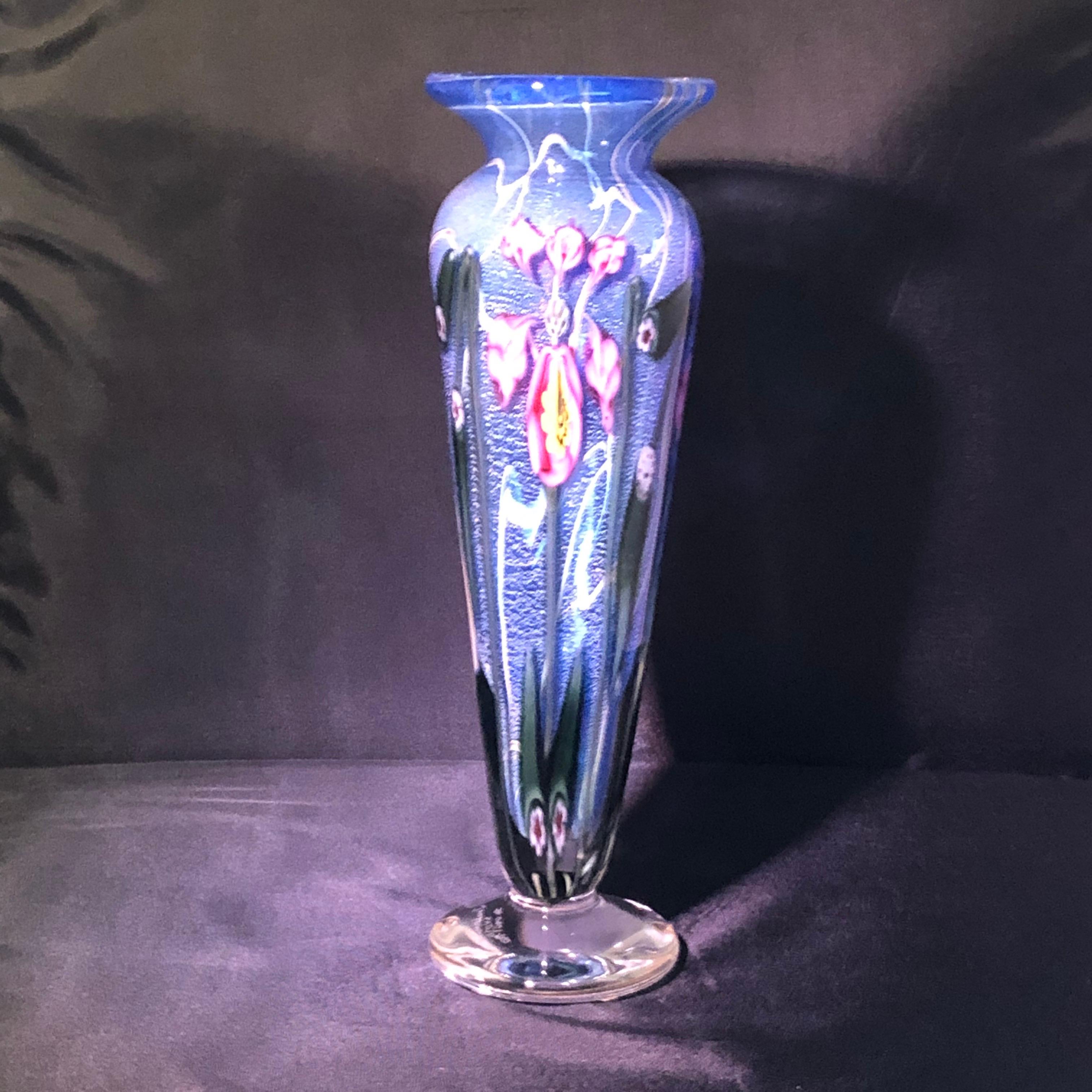 Hand blown Vandermark art glass vase decorated with beautiful pink exotic flowers on a blue colored background. It was hand blown so when the light hits it, you can see beautiful shimmering gold speckles throughout the vase. The vase is signed by