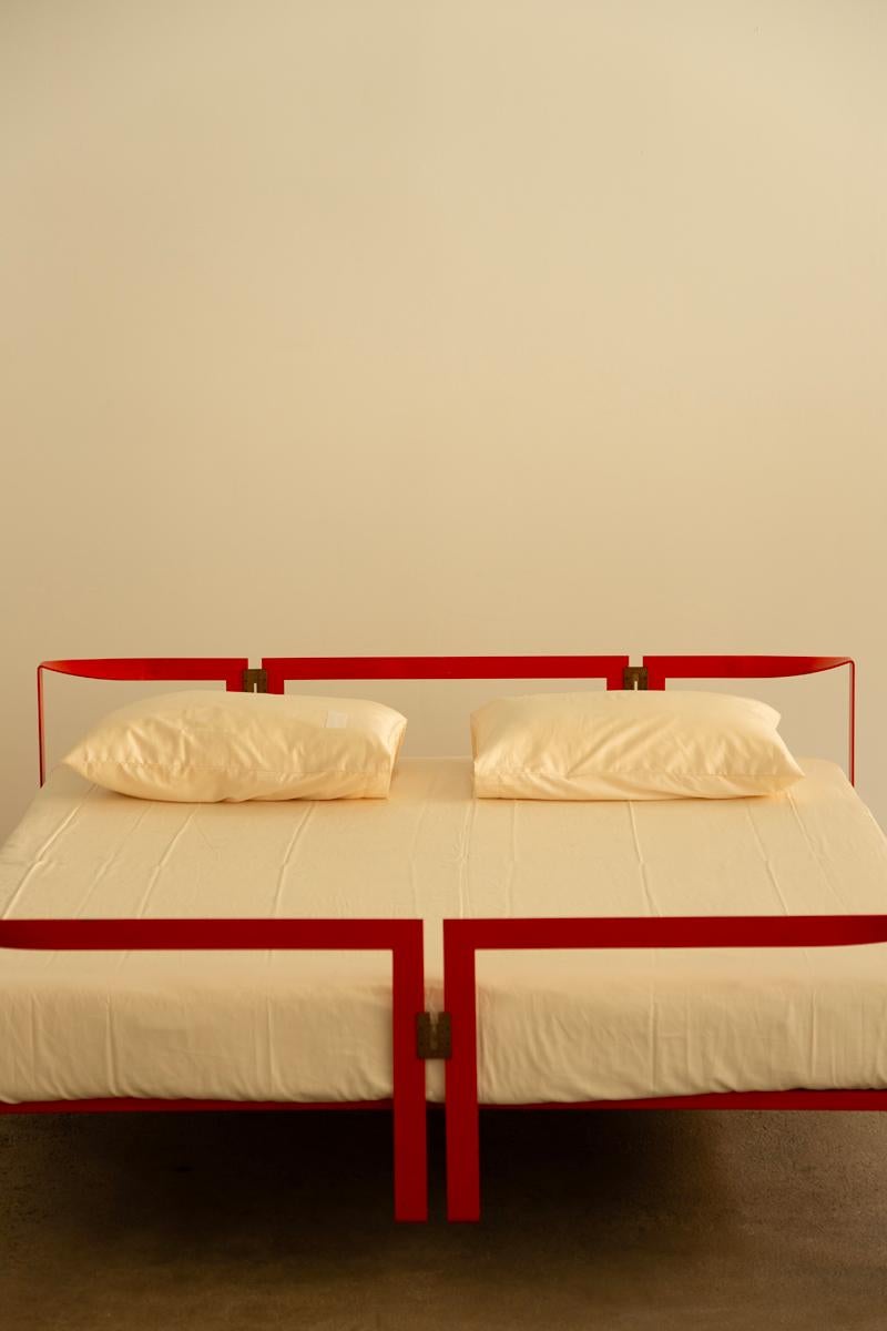 Striking bed design featuring a powder-lacquered metal frame in bold China red. The structure includes a matching headboard and footrest, with the support frame and base constructed from tubular metal. Stainless steel linking elements add a refined,