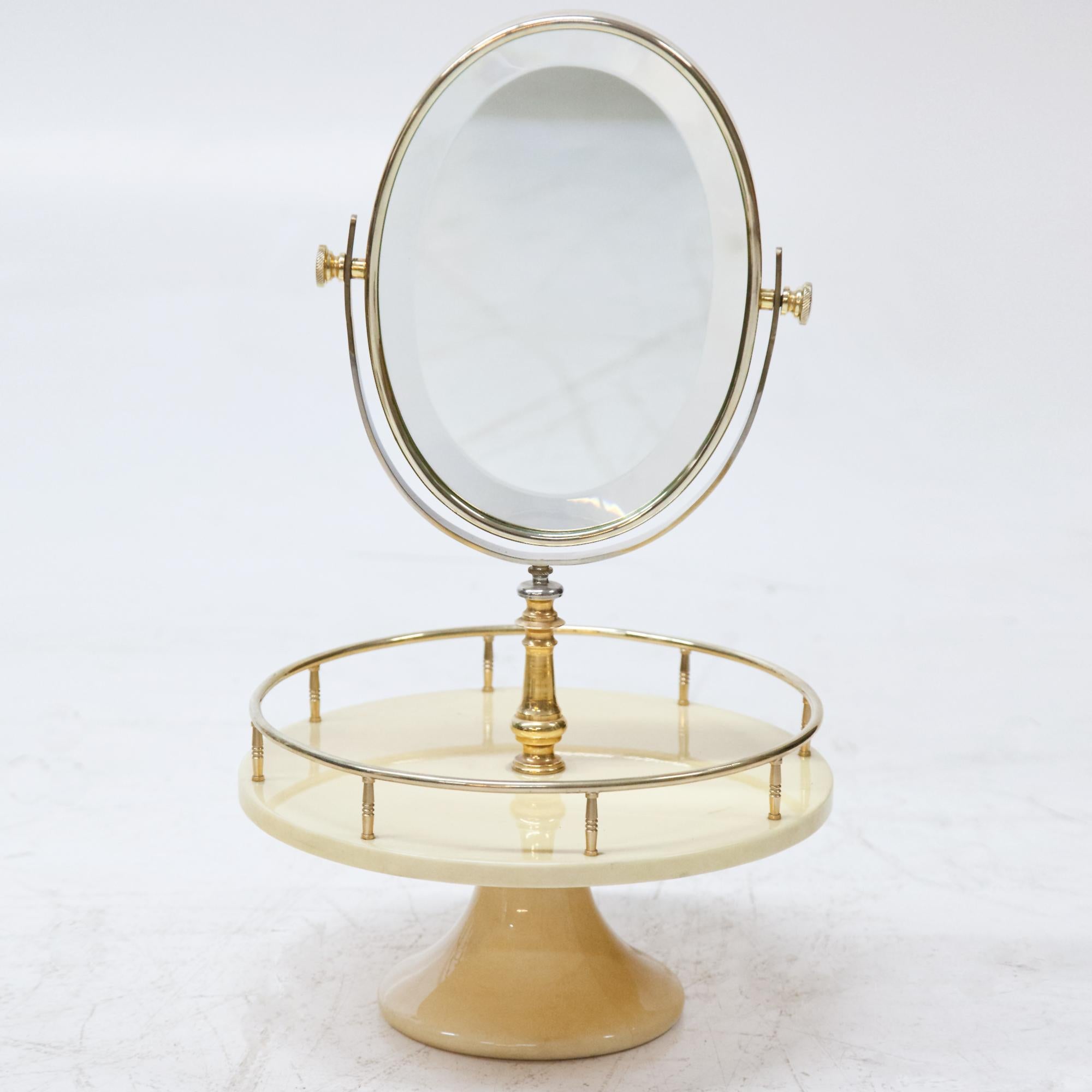 Oval mirror standing on round base with brass balustrade. The two-sided mirror is slightly faceted at the edge and can be tilted and rotated. The stand is covered with beige goatskin and clear lacquer.