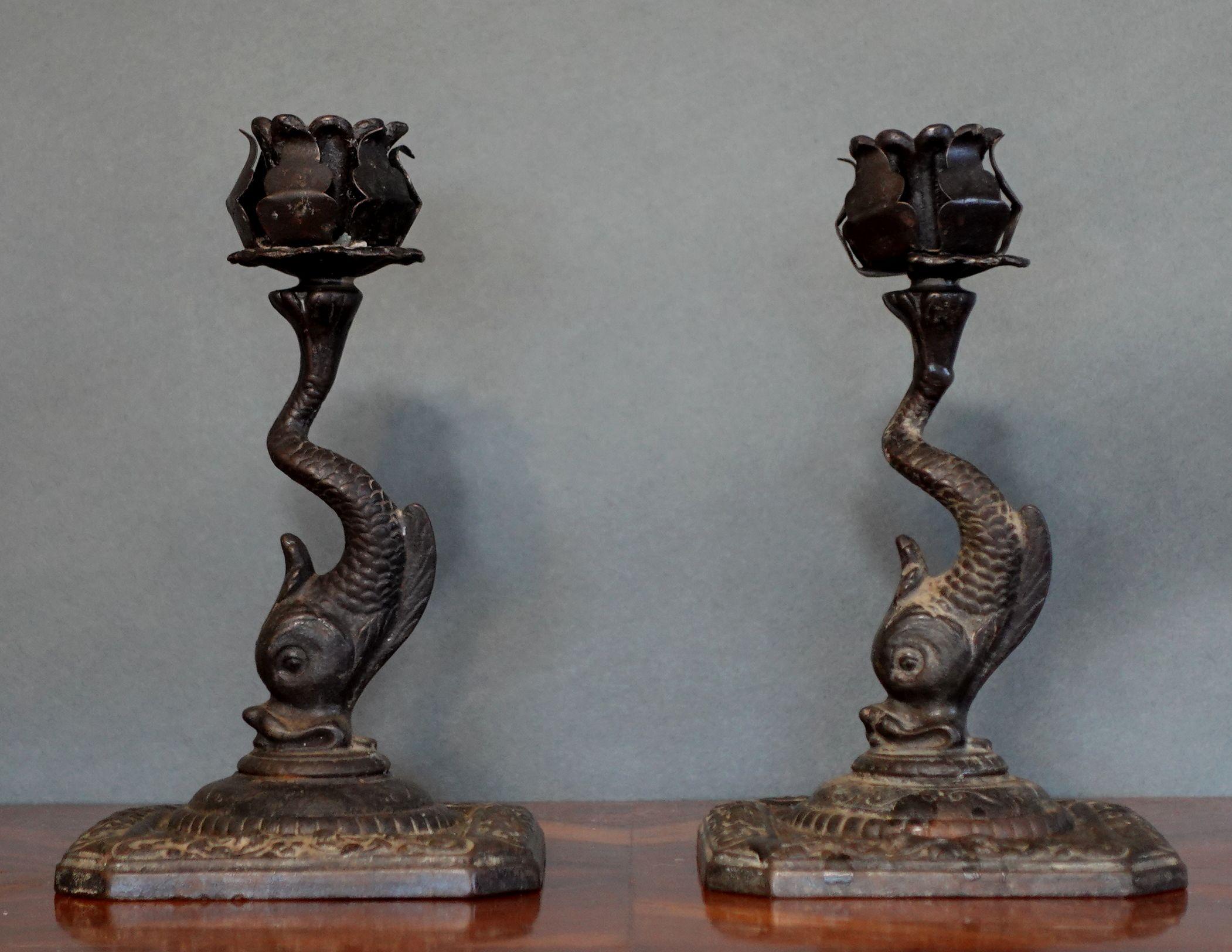A pair of candlesticks made of wrought iron with flower shapes at the top of each holder.
Under the flower heads, there are winding fish shapes below and the fish heads attached to the square bases.
Very old pieces and unique art pieces.