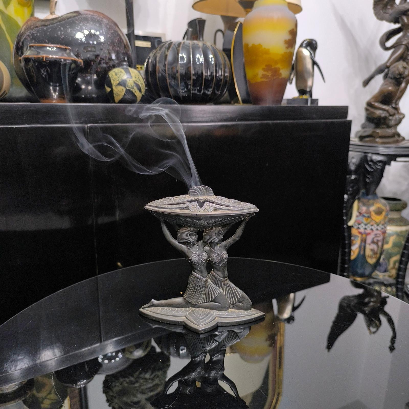 Bruciatore di incenso in metallo fuso in stile Art Déco francese di Vantines con motivo egiziano, con il modello di due eleganti dame egiziane inginocchiate che sorreggono la camera dell'incensiere. 
Dimensioni: 18x8,5x18 cm 
Marcato: Vantines Made