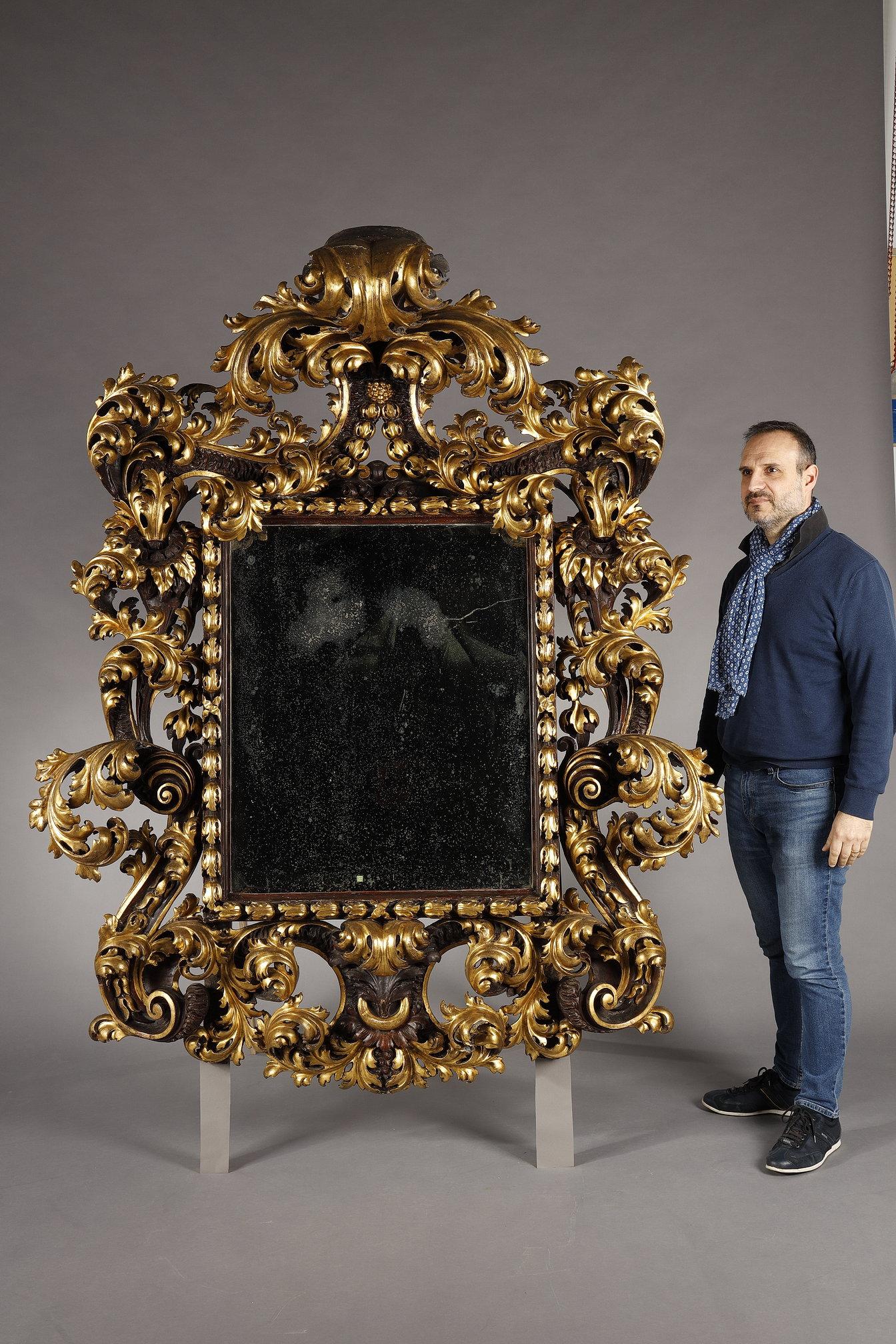 Very important mirror frame in carved, gilded and patinated wood with rich acanthus leaf and scroll decoration in beautiful symmetry around a rectangular frame containing a silver mercury mirror.

Italian work, particularly Roman, from the late 17th