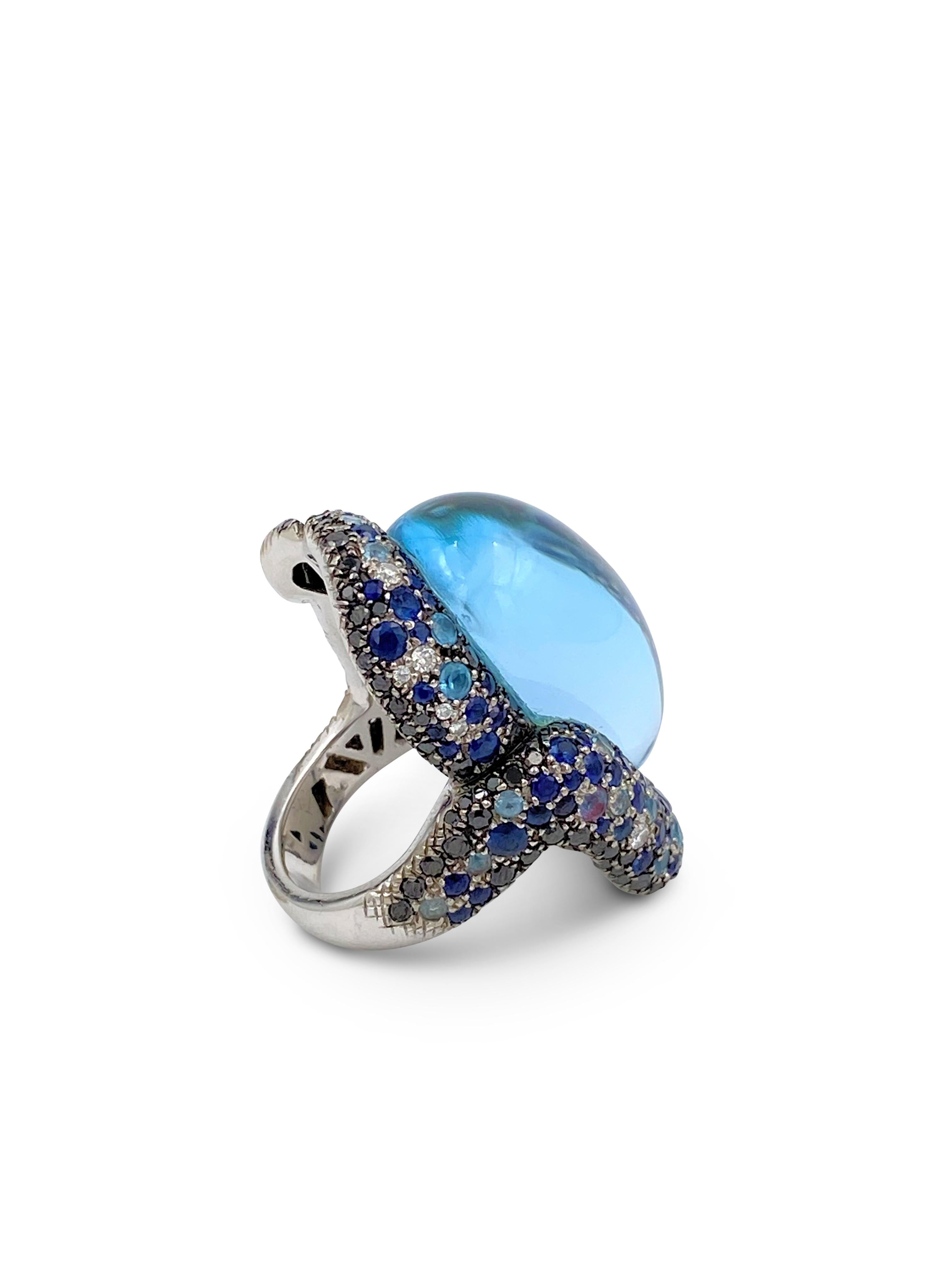 A bold Vasari cocktail ring crafted in 18 karat white gold featuring a cabochon blue topaz stone and set with an estimated 3.00 carats of sapphires as well as black and white diamonds weighing approximately 2.50 carats. Signed Vasari with hallmarks.