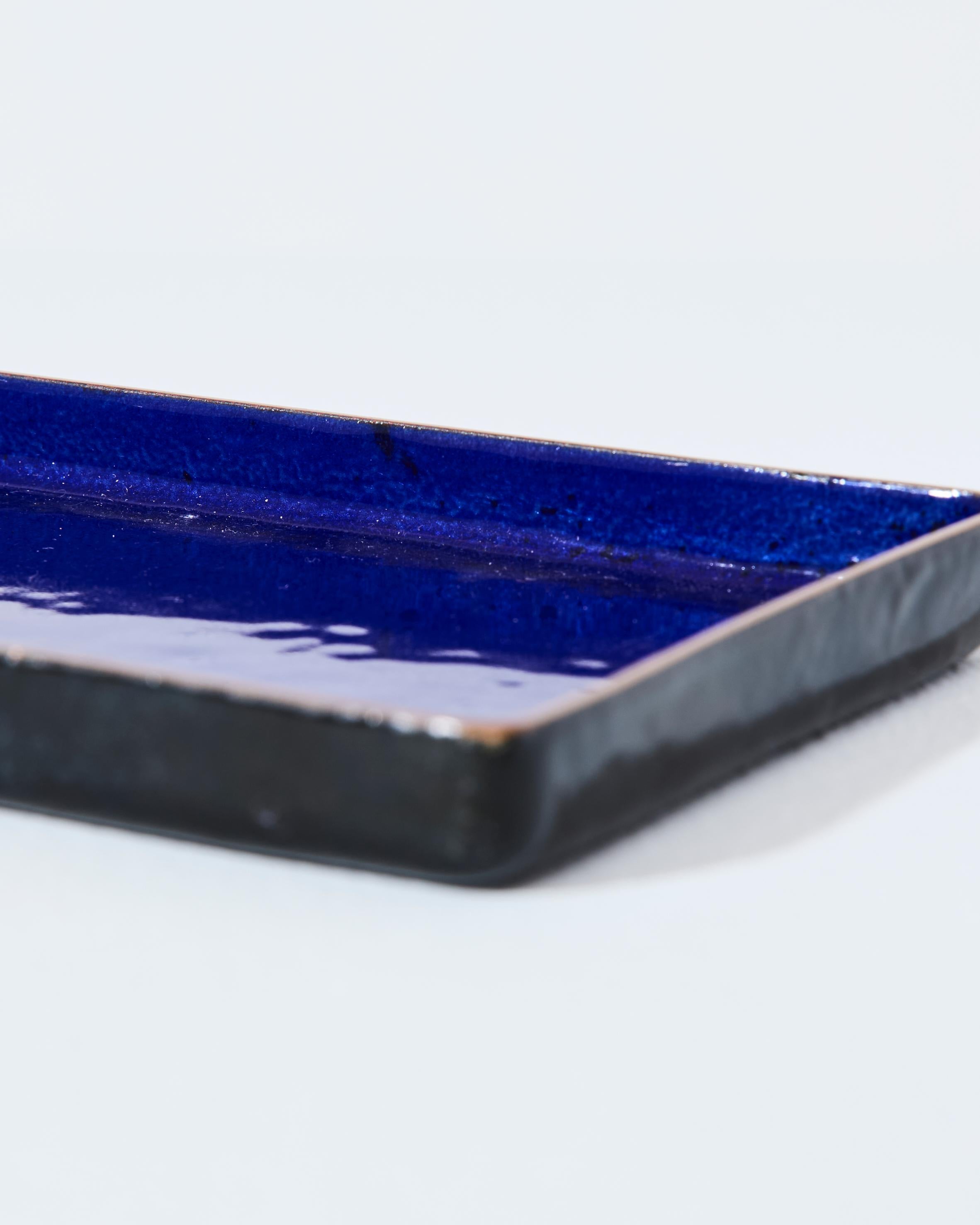 Elegante bandeja rectangular de cobre esmaltado creada por el famoso artista y maestro esmaltador Paolo De Poli. Italia, año 1960. La superficie está recubierta de un esmalte azul cobalto intenso, que contrasta con el borde de cobre visto, para