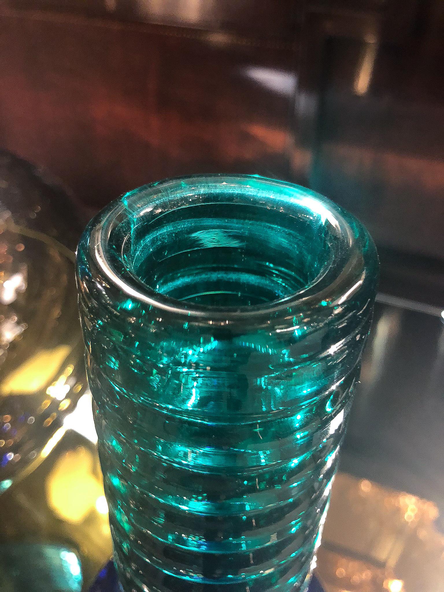 Vaso in vetro soffiato a mano con un corpo blu trasparente e un collo alto a bande di colore verde trasparente.

IL NOSTRO RIFERIMENTO N9437