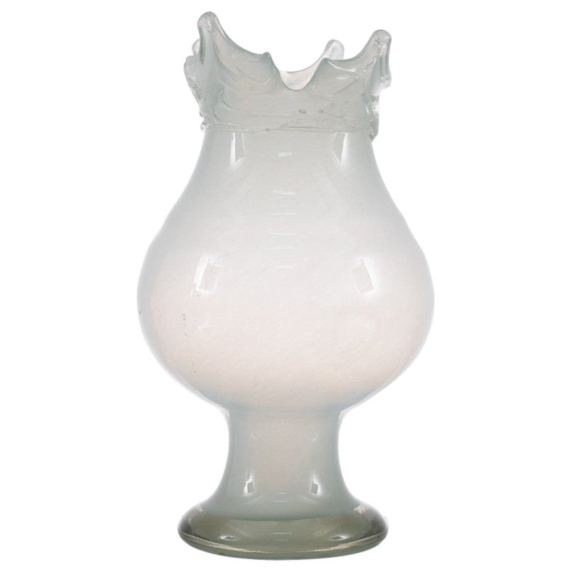 Produzione Italia 1960 ca.
Vaso in vetro lattimo, corpo ovalizzato su piede cilindrico, bocca a punte con decoro a fili lungo il collo, base circolare.
Lavorazione in vetro soffiato.
in questo periodo divenne la Vetreria di famiglia e che si