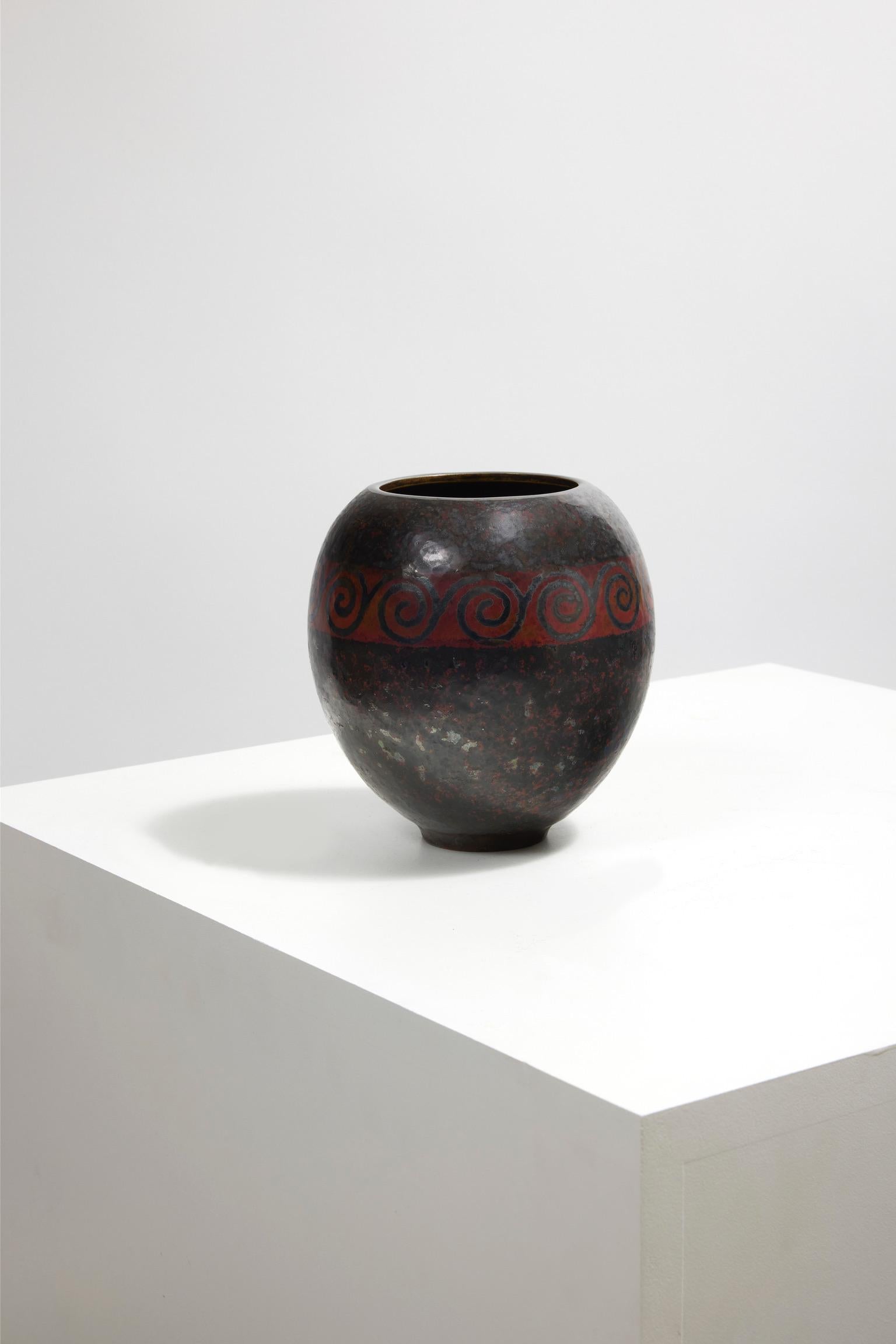 Ovoid vase in copper brassware hammered decorated with a horizontal geometric frieze of spirals inlaid in maillechort on a red background with brown patina.

Signature in hollow on the back and dated 