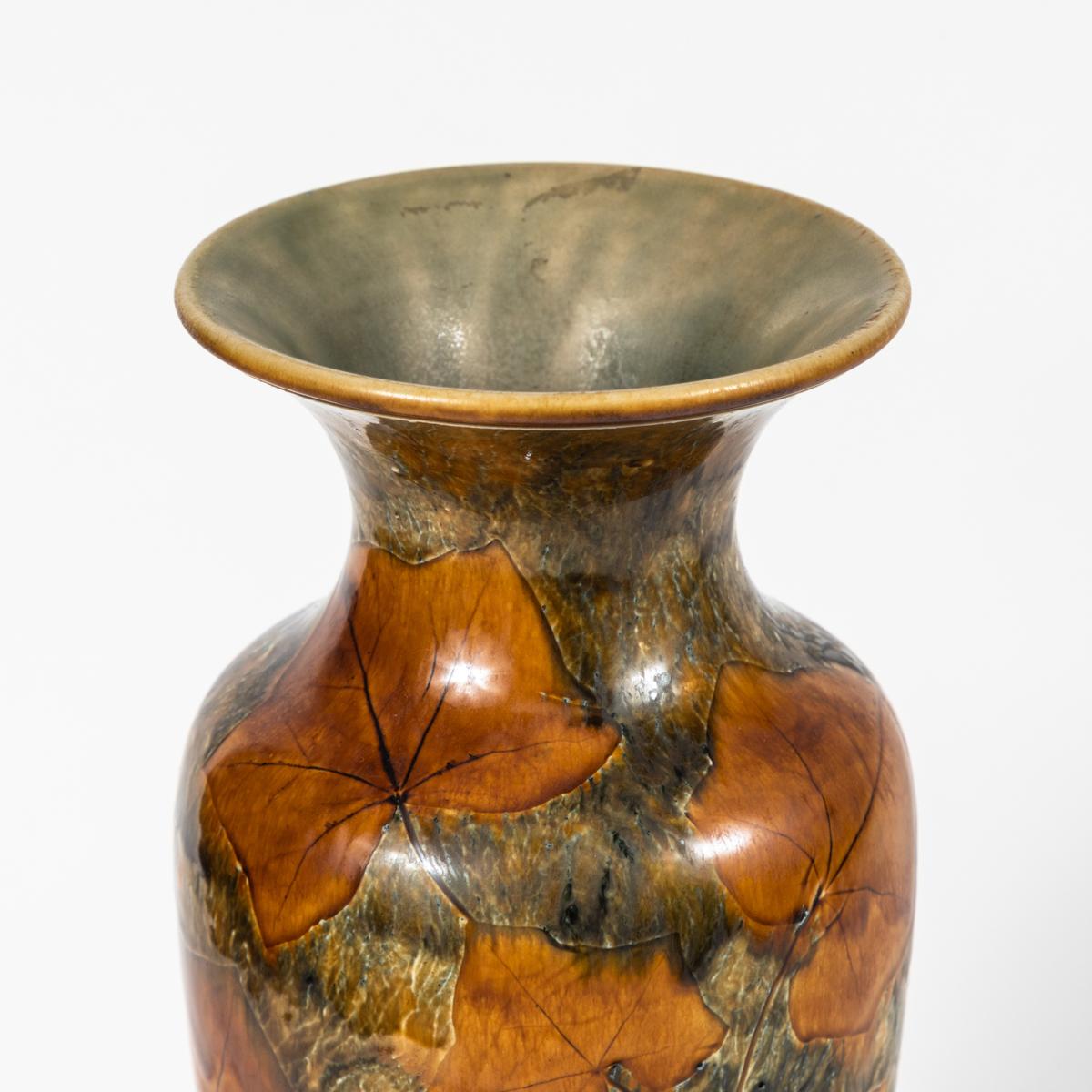 Tall early 20th-century vase by Royal Doulton featuring a leaf motif in earthy shades of persimmon, olive, and moss. With a fluted aperture and raised circular base, the vessel has a classic, well-balanced shape. 

England, 1900

Dimensions: 6.5W x