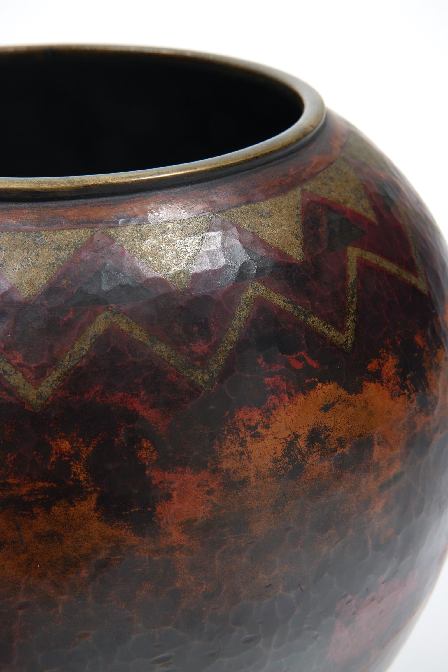 Spherical vase on light heel and with a wide annular neck. 
Proof in copperware mounted with a hammer.
Decoration realized with fire patina and silver inlays on a background, also fire patinated, red richly shaded with ochre and anthracite.